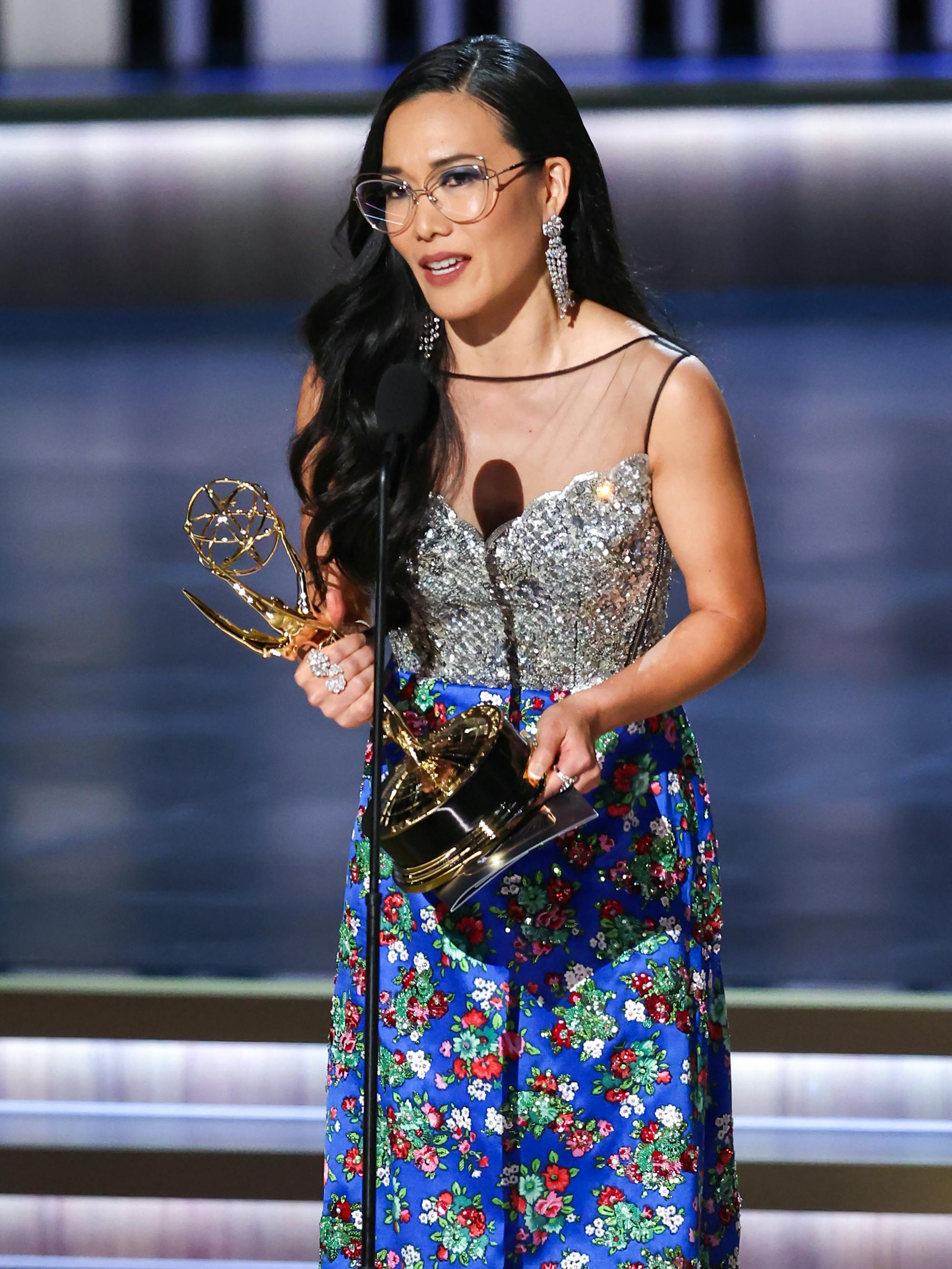 Ali Wong wears a patterned blue dress and clutches her Emmy. 