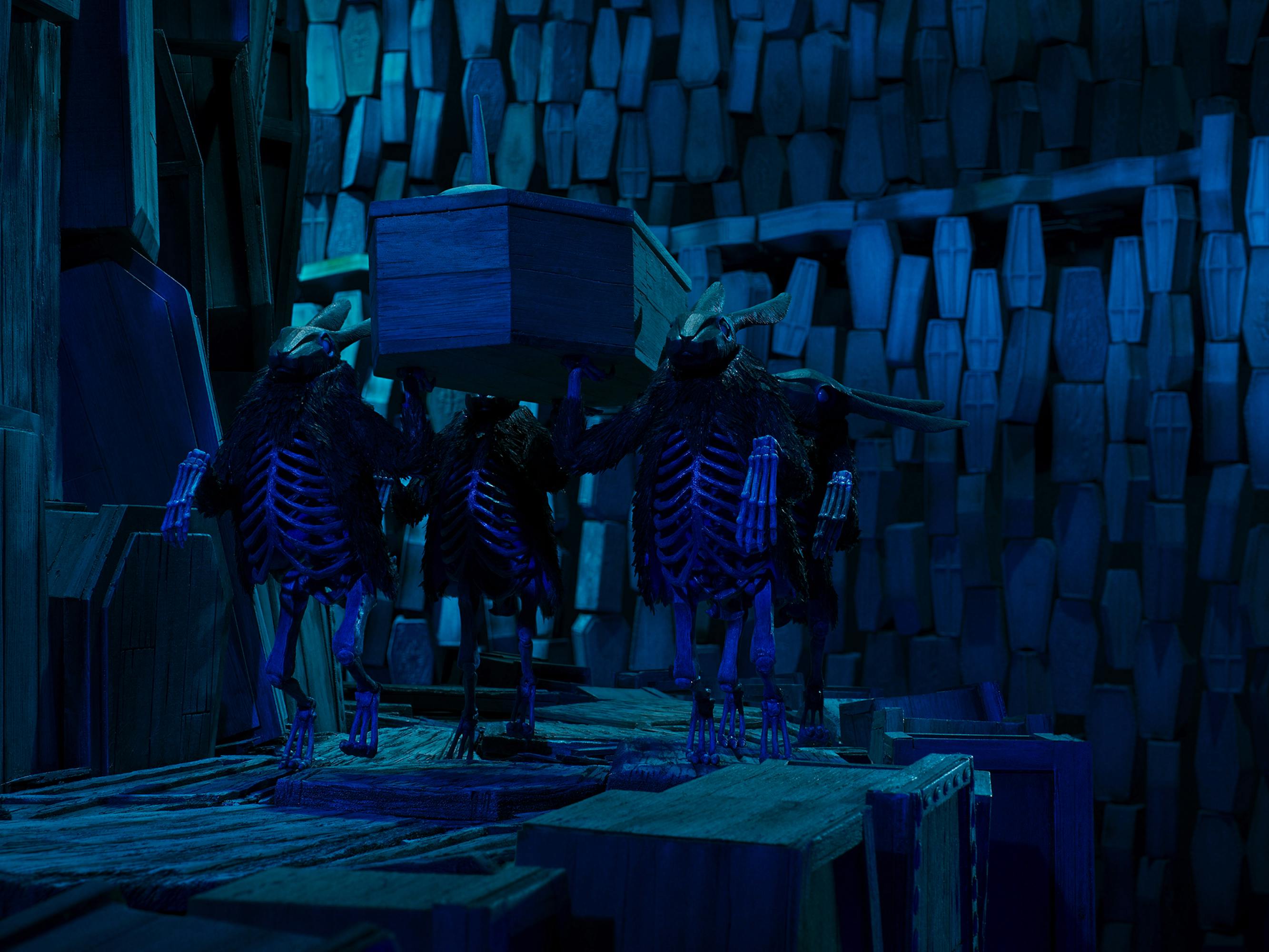 The Black Rabbits (Tim Blake Nelson) carry a coffin through a blue-black lit scene.