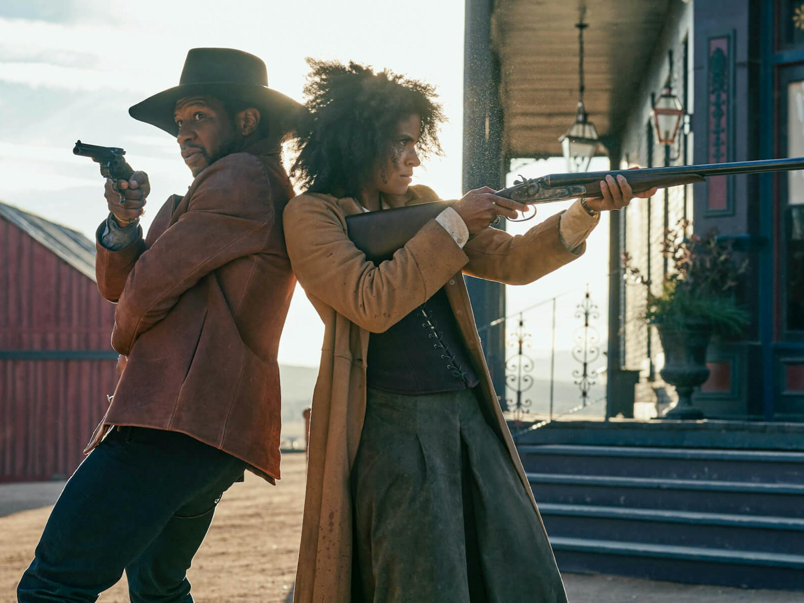 Nat Love (Jonathan Majors) and Stagecoach Mary Fields (Zazie Beetz) stand back to back, their guns at the ready. They both wear brown jackets. Mary carries a long rifle and Majors holds a pistol.