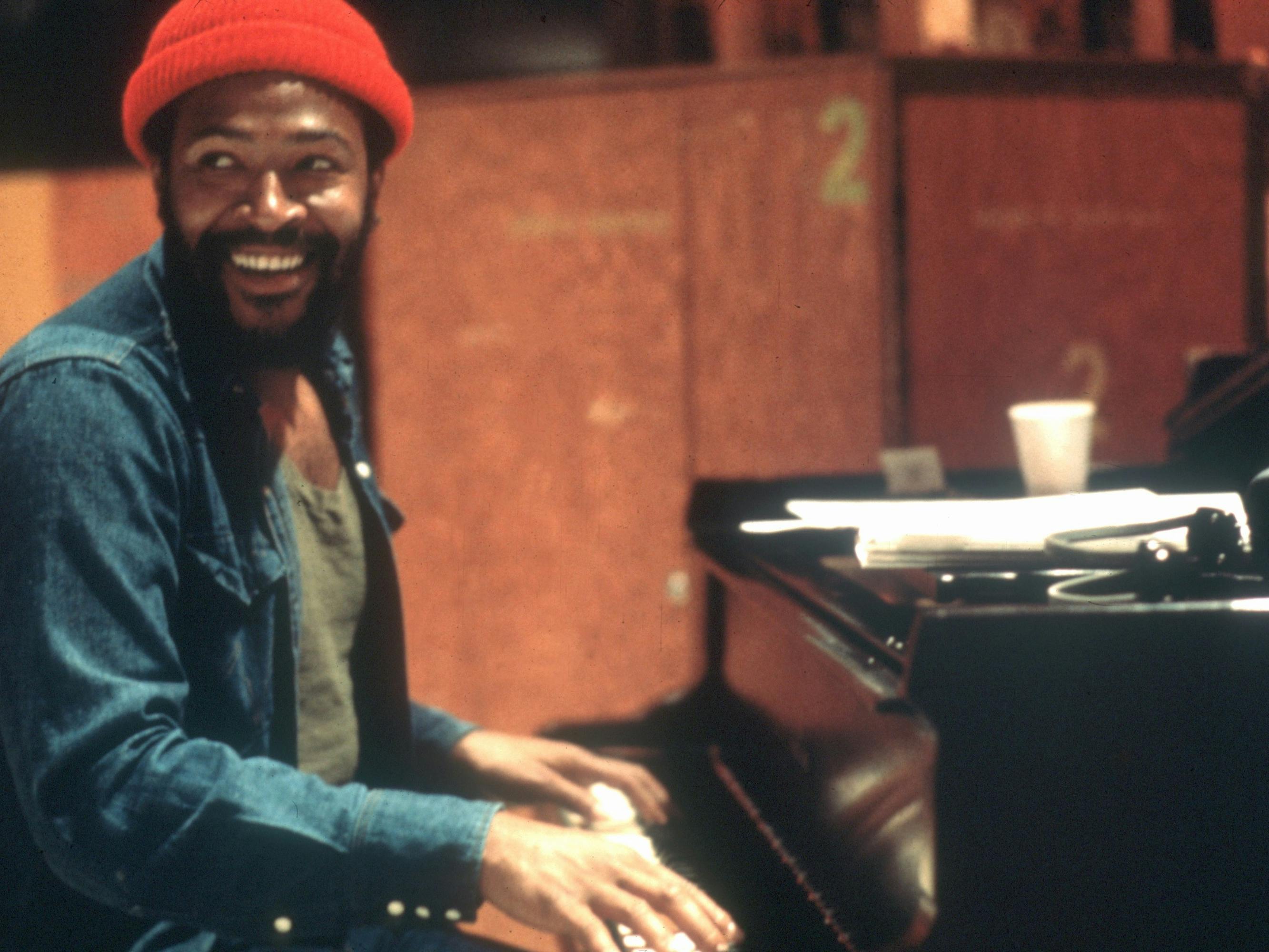 Marvin Gaye at Golden West Studios in 1973 in Los Angeles, California wears a red beanie and jean shirt and plays piano.