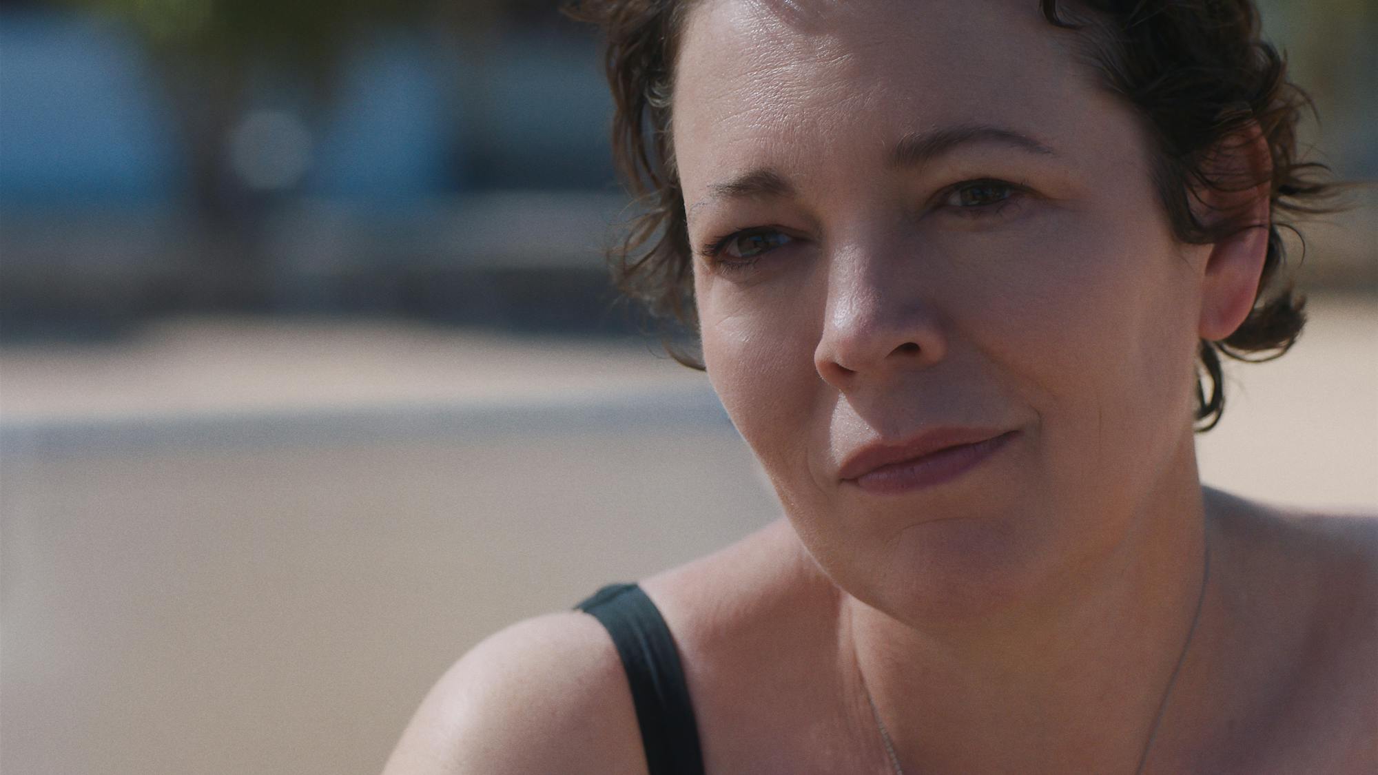 Olivia Colman wears a black bathing suit and smiles in the sunshine. 