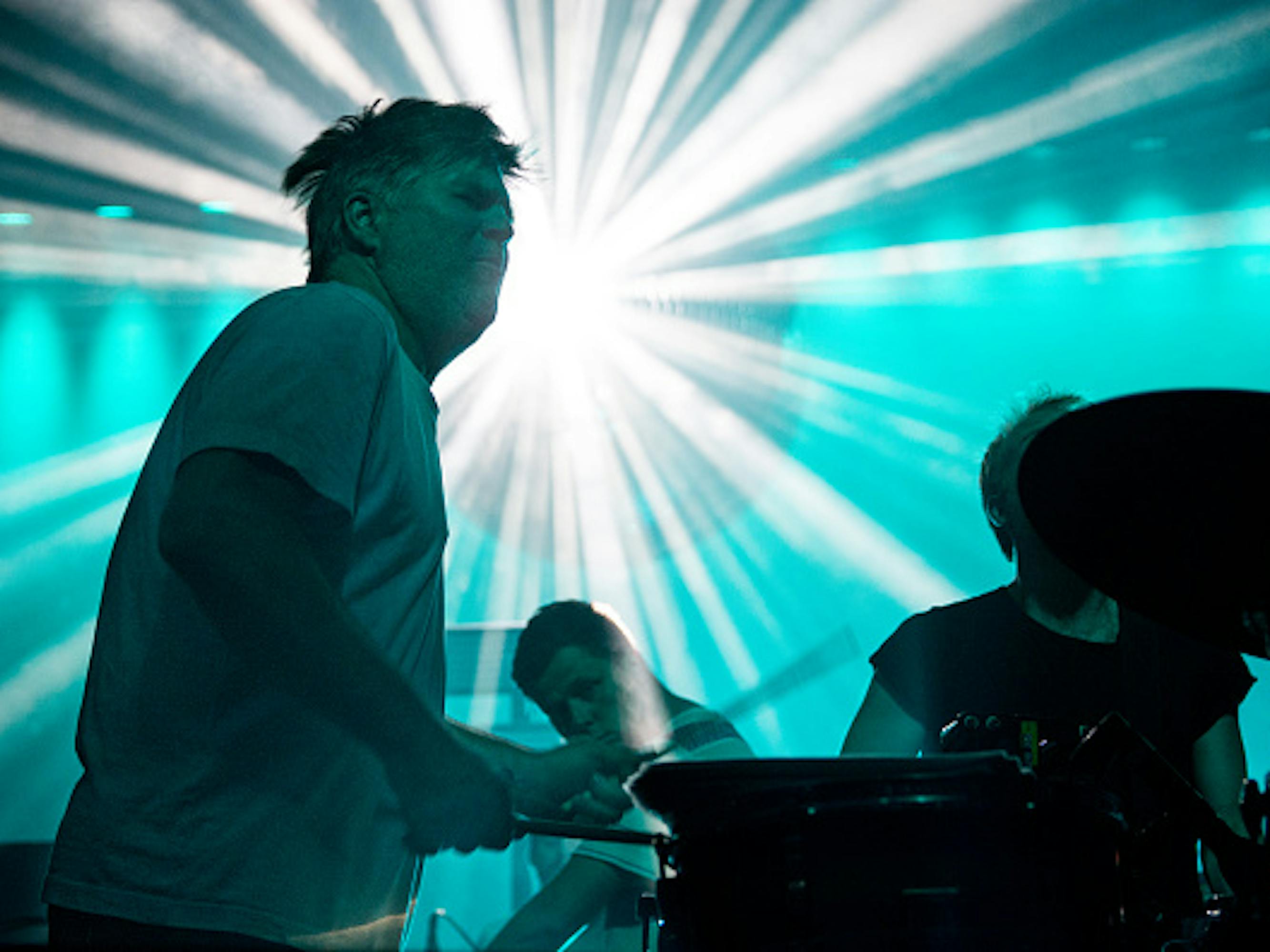 LCD Soundsystem plays the drums against a bright light.