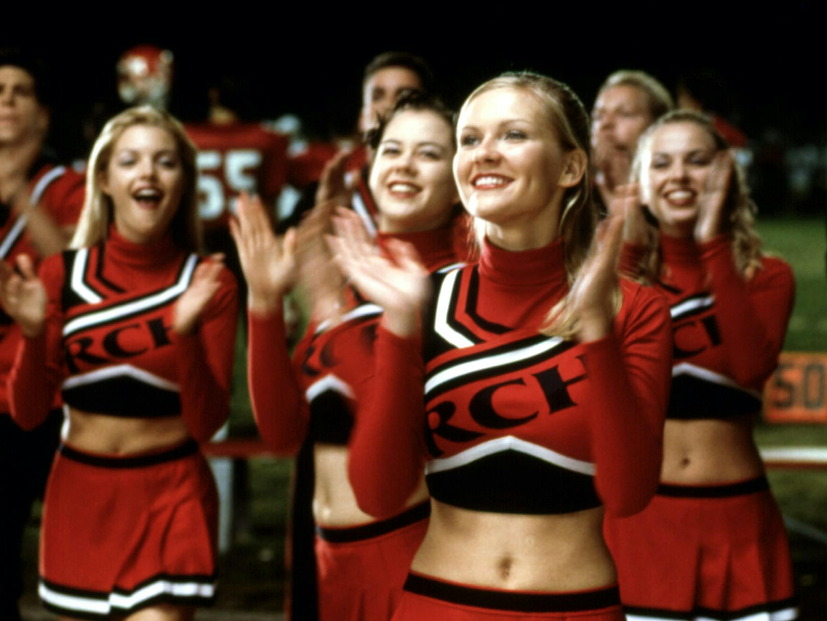 Torrance Shipman (Kirsten Dunst) cheers along with the rest of the cheerleading squad in red, black, and white uniforms.