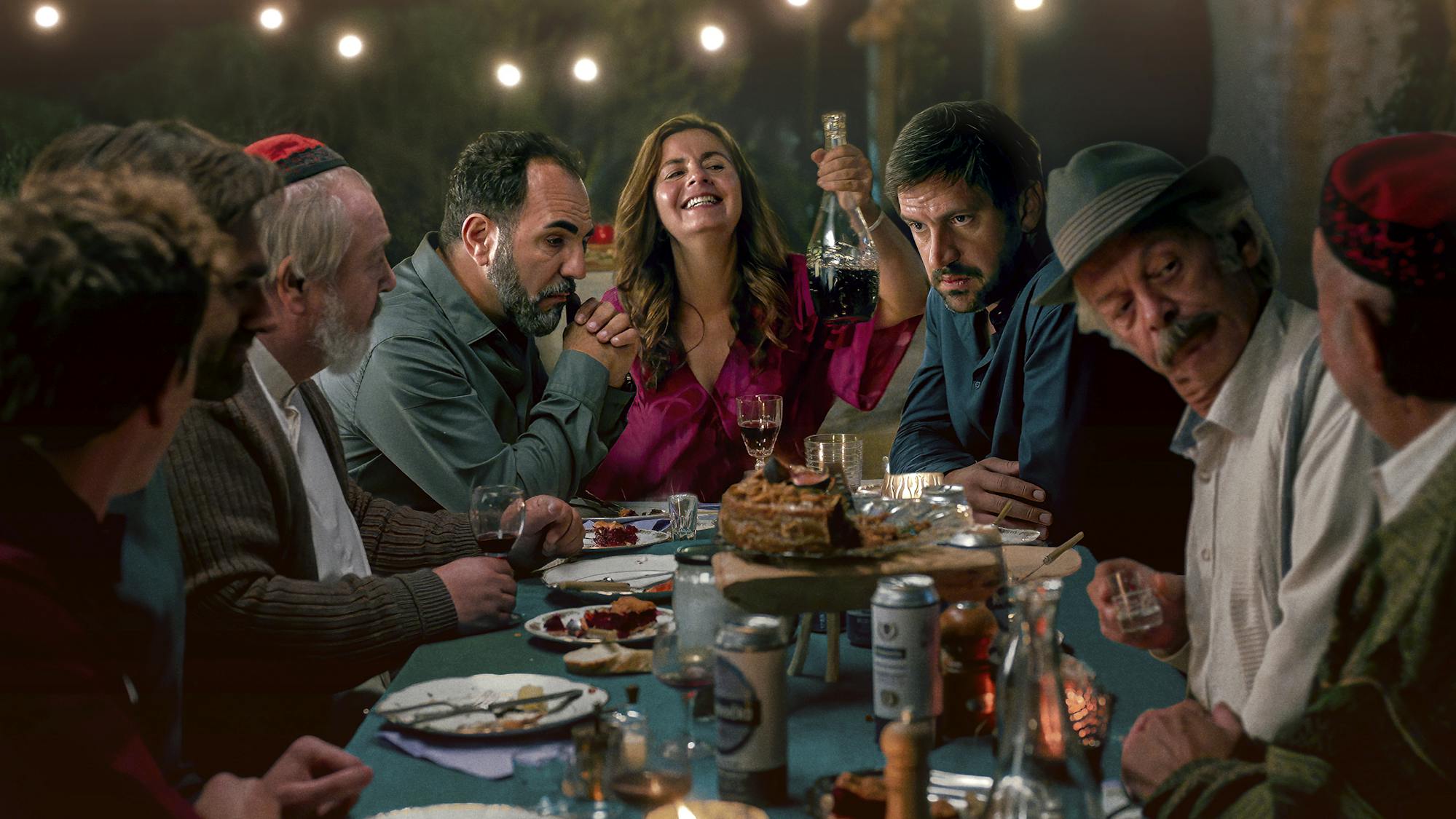Ilyas Altin (Adnan Maral), Zeynep (Naomi Krauss), Josip (Goran Bogdan) sit together at a very full dinner table, laughing and talking.