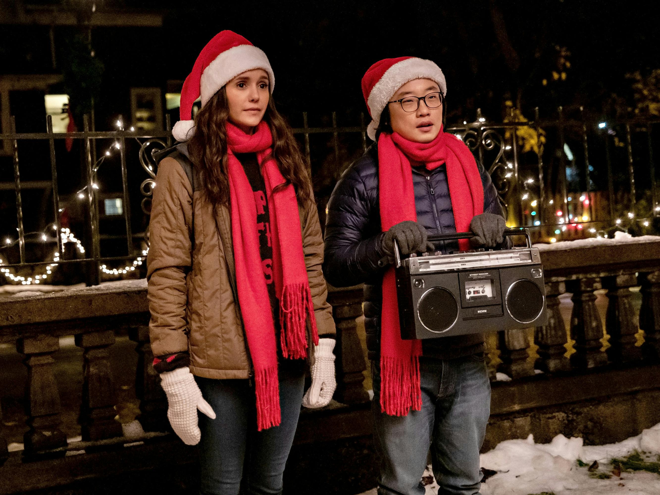 Natalie Bauer (Nina Dobrev) and Josh Lin (Jimmy O. Yang) sit together with a stereo, wearing red scarves and santa hats.