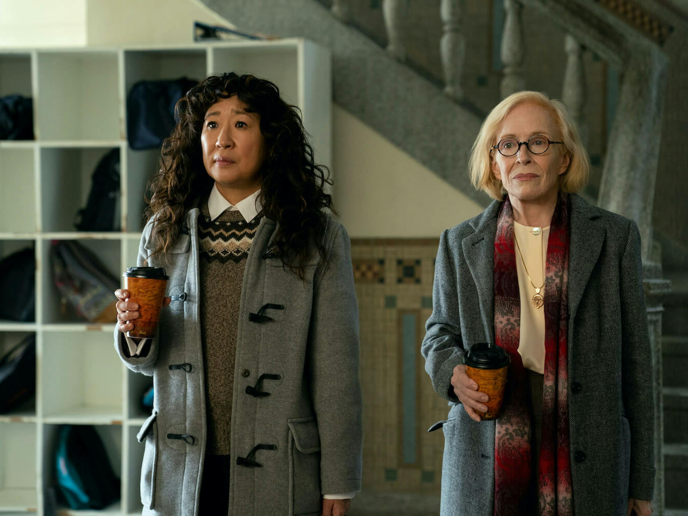 Dr. Ji-Yoon Kim (Sandra Oh) and Professor Joan Hambling (Holland Taylor) wear wool coats and sweaters and hold coffee to-go cups.
