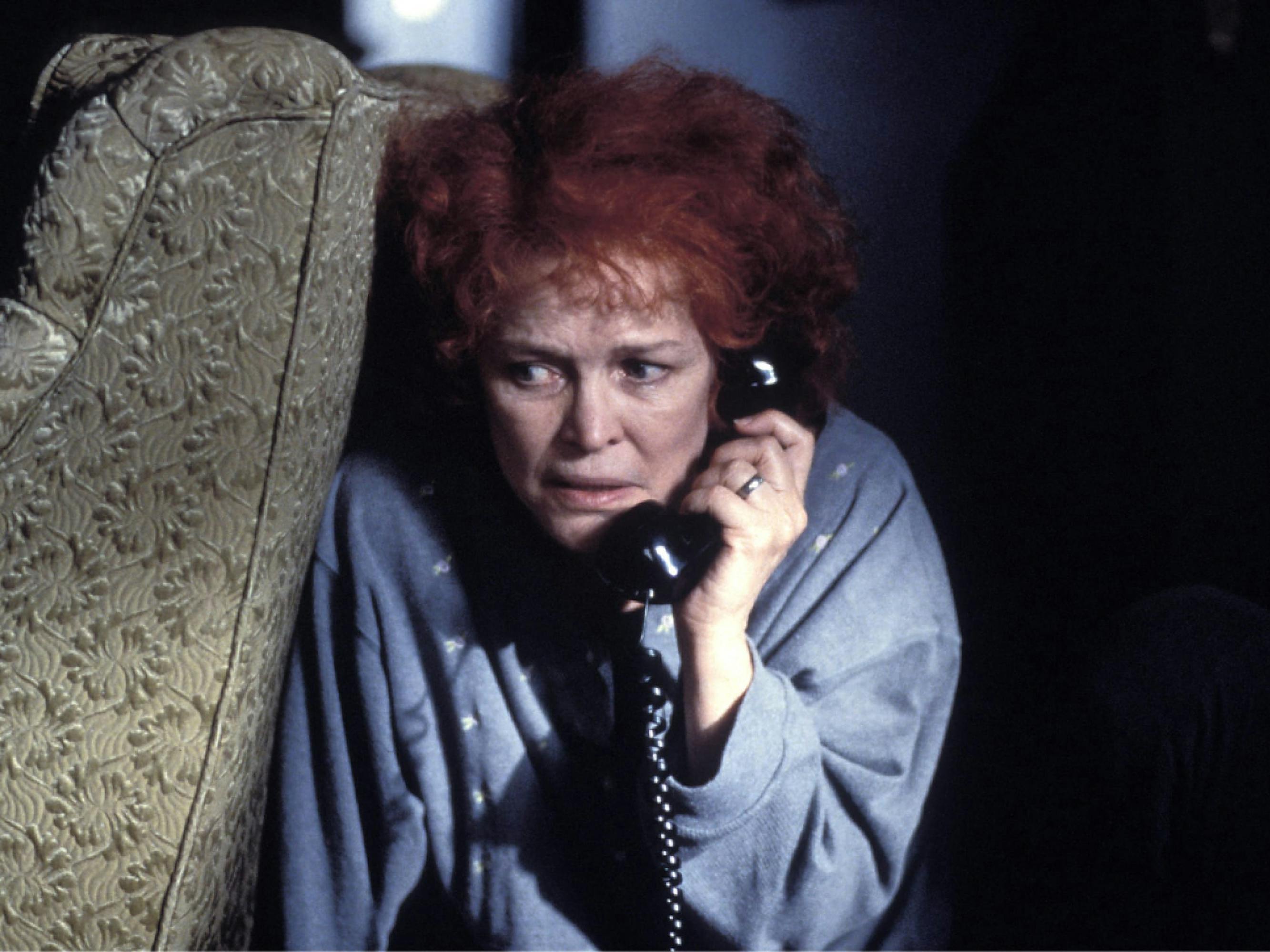 Ellen Burstyn as Sara Goldfarb in Requiem for a Dream. She’s crouched in fear behind upholstered furniture, gripping a phone to her ear, which is covered by an explosion of frizzy red hair.