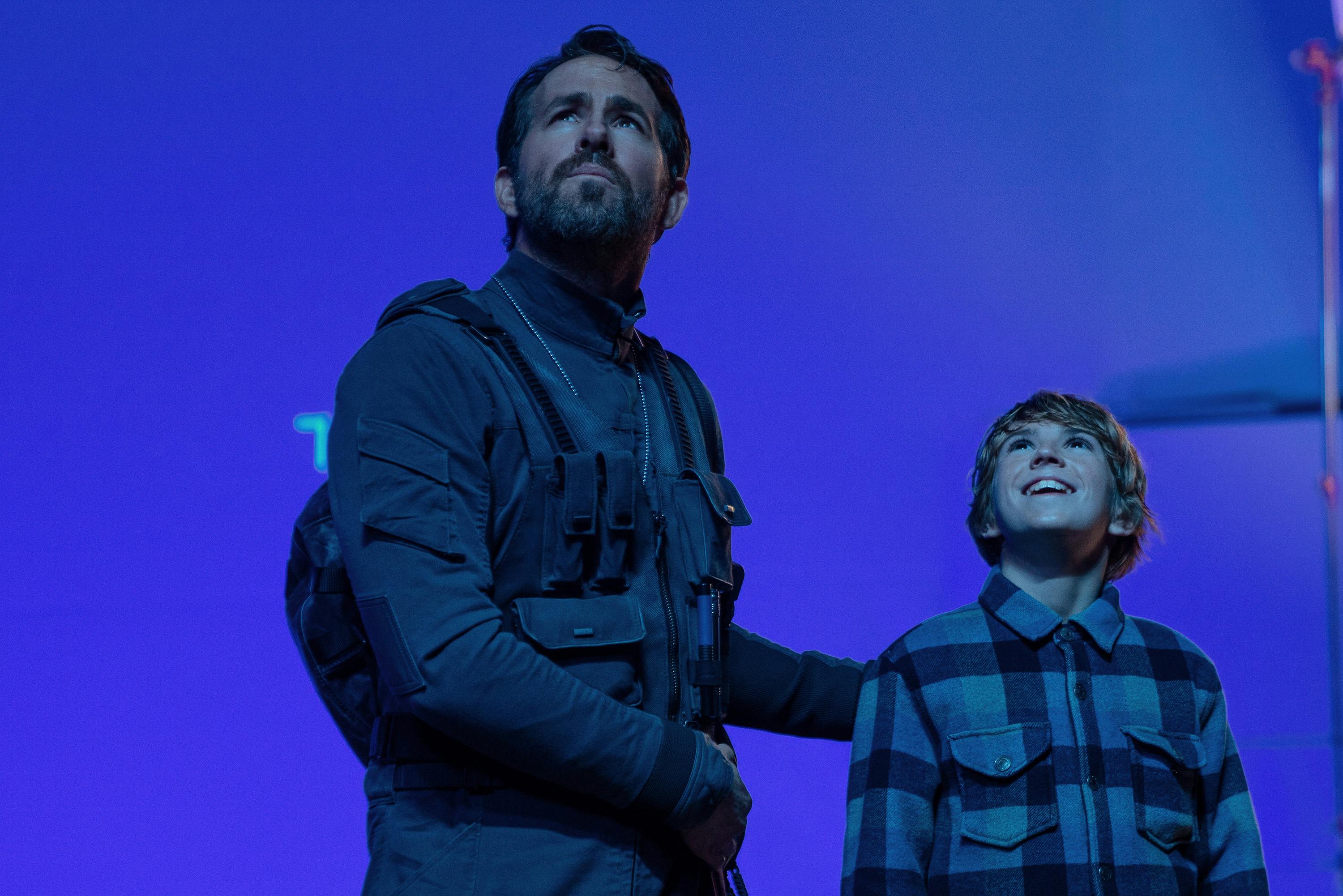 The Adam Project's Ryan Reynolds as Big Adam and Walker Scobell as Young Adam are on the set of the epic time-travel film with a blue screen behind them.