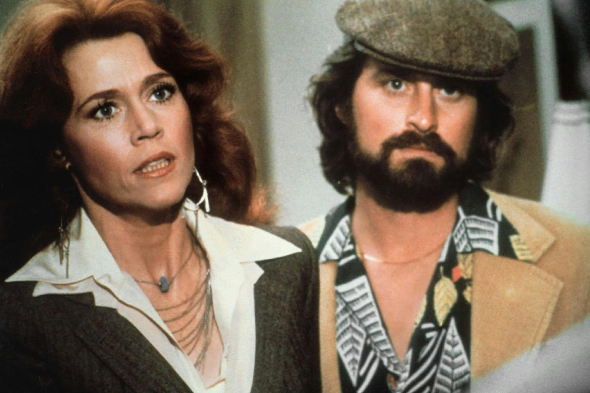 Kimberly Wells (Jane Fonda) and Richard Adams (Michael Douglas) in The China Syndrome. Fonda wears a brown blazer and white collared shirt, while Douglas wears a messenger hat, and tan blazer.