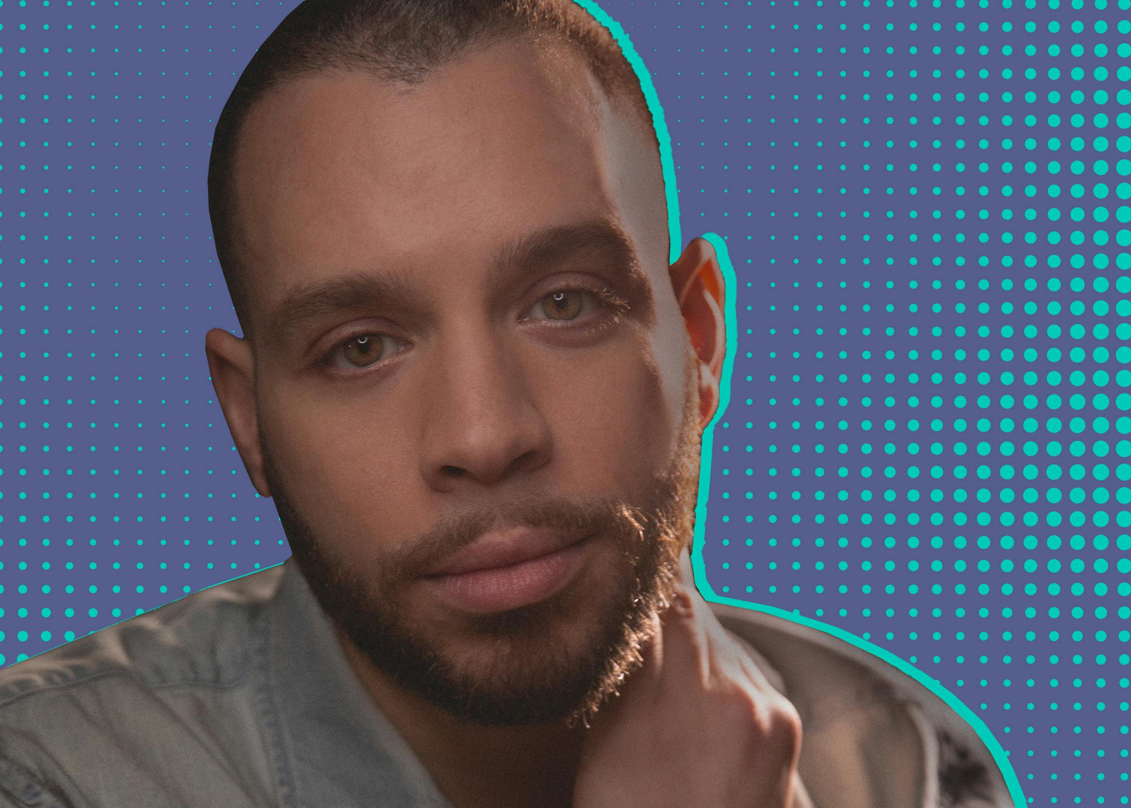 Robin de Jesús wears a grey shirt and looks softly at the camera. Behind him is a teal and purple polka-dotted background.