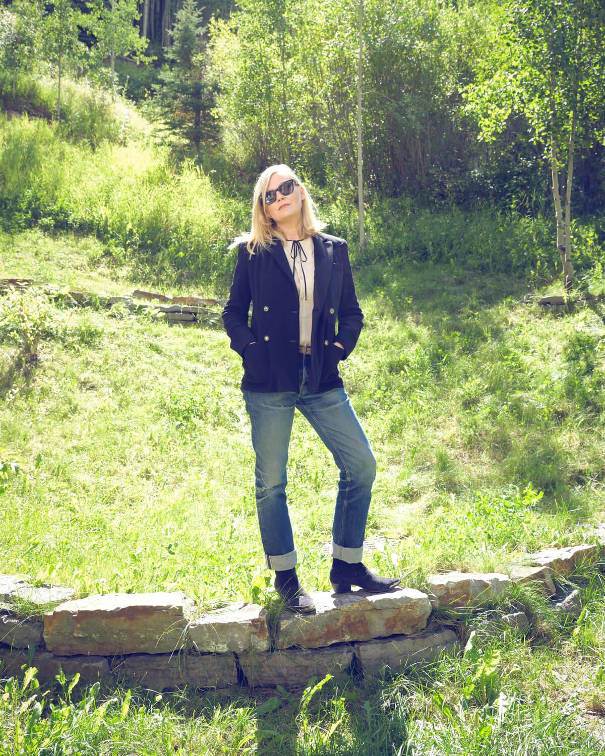 Kirsten Dunst in a double-breasted blazer, blouse, jeans and boots in the woods of the Colorado mountains at the Telluride Film Festival, 2021.
