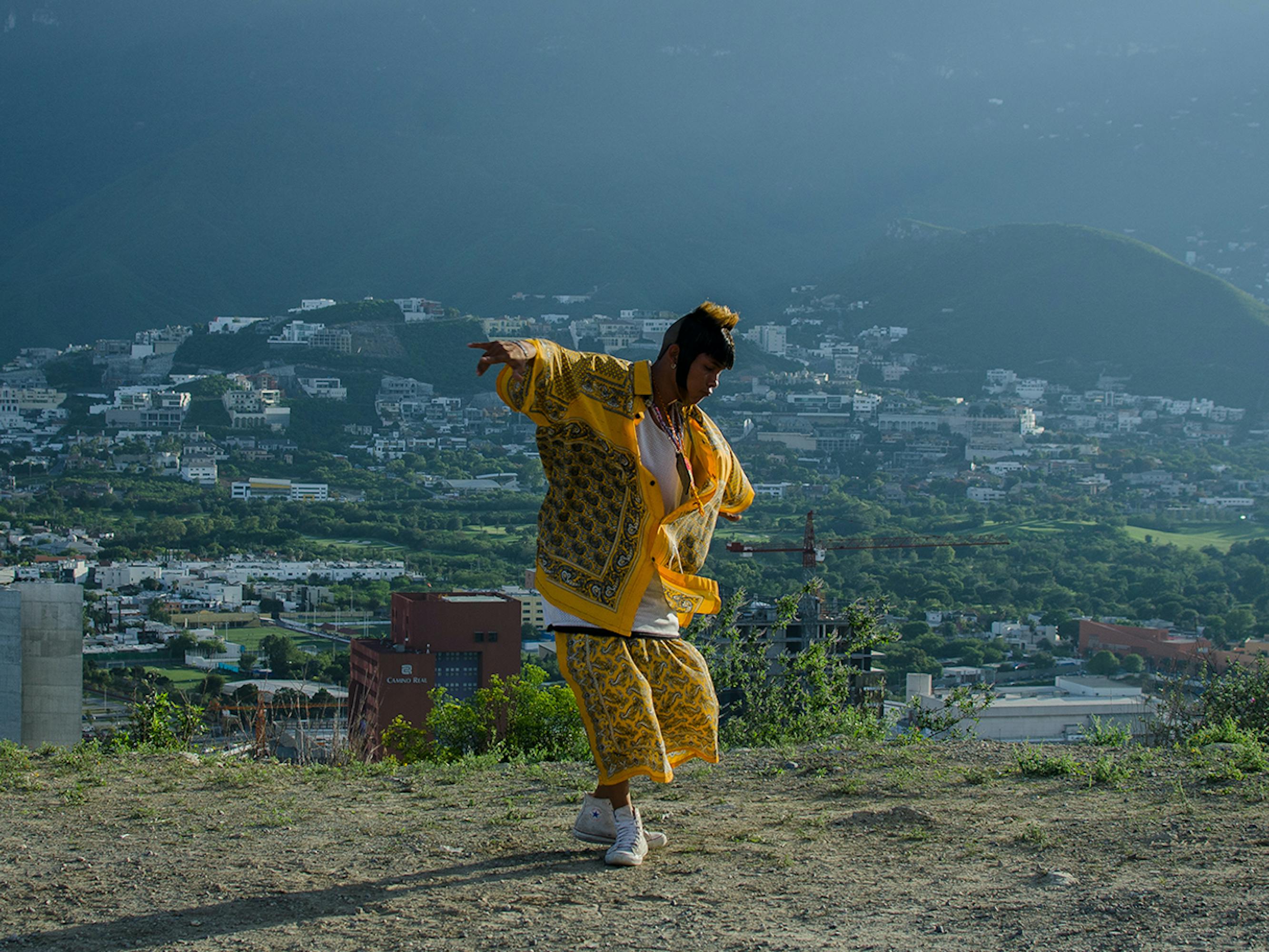 The main character from I’m No Longer Here dances to cumbia music in a yellow outfit. 