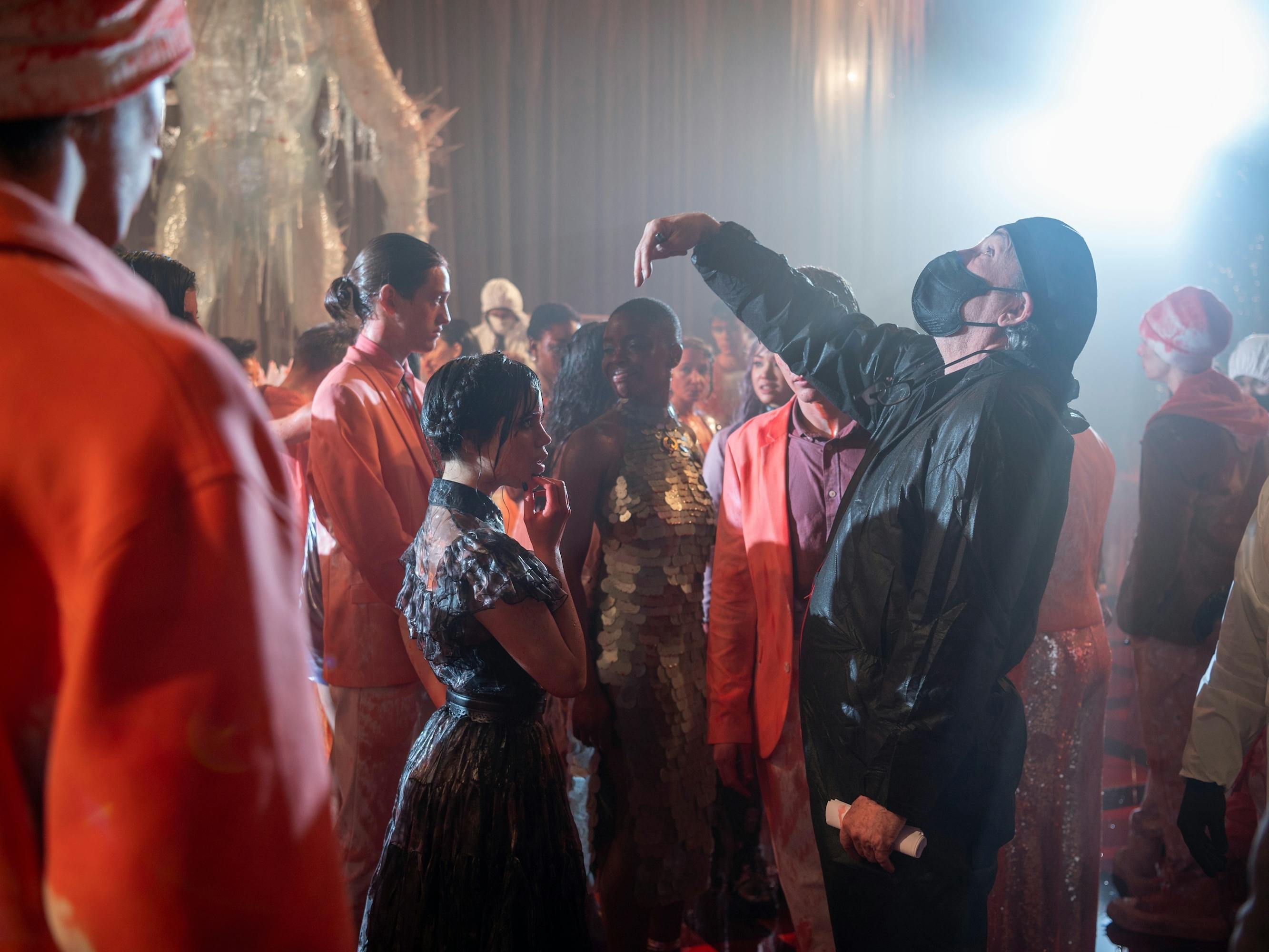 Wednesday Addams (Jenna Ortega) stands next to Tim Burton in a sea of people drenched in fake blood.