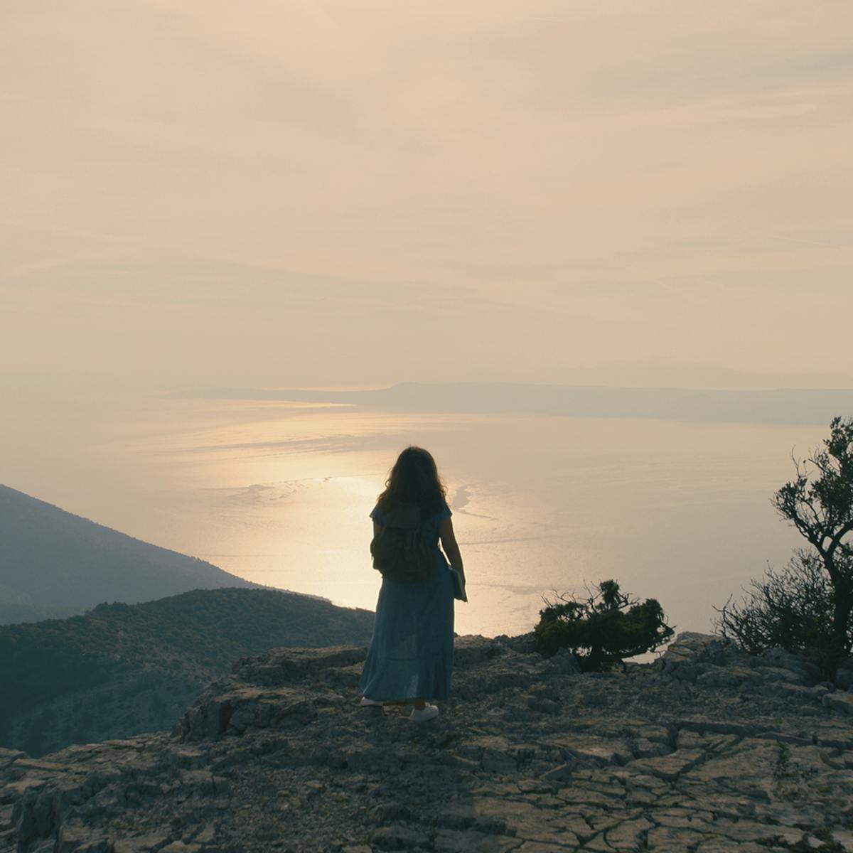 Zeynep (Naomi Krauss) stands on a cliff’s edge overlooking a beautiful sun setting on the still water.