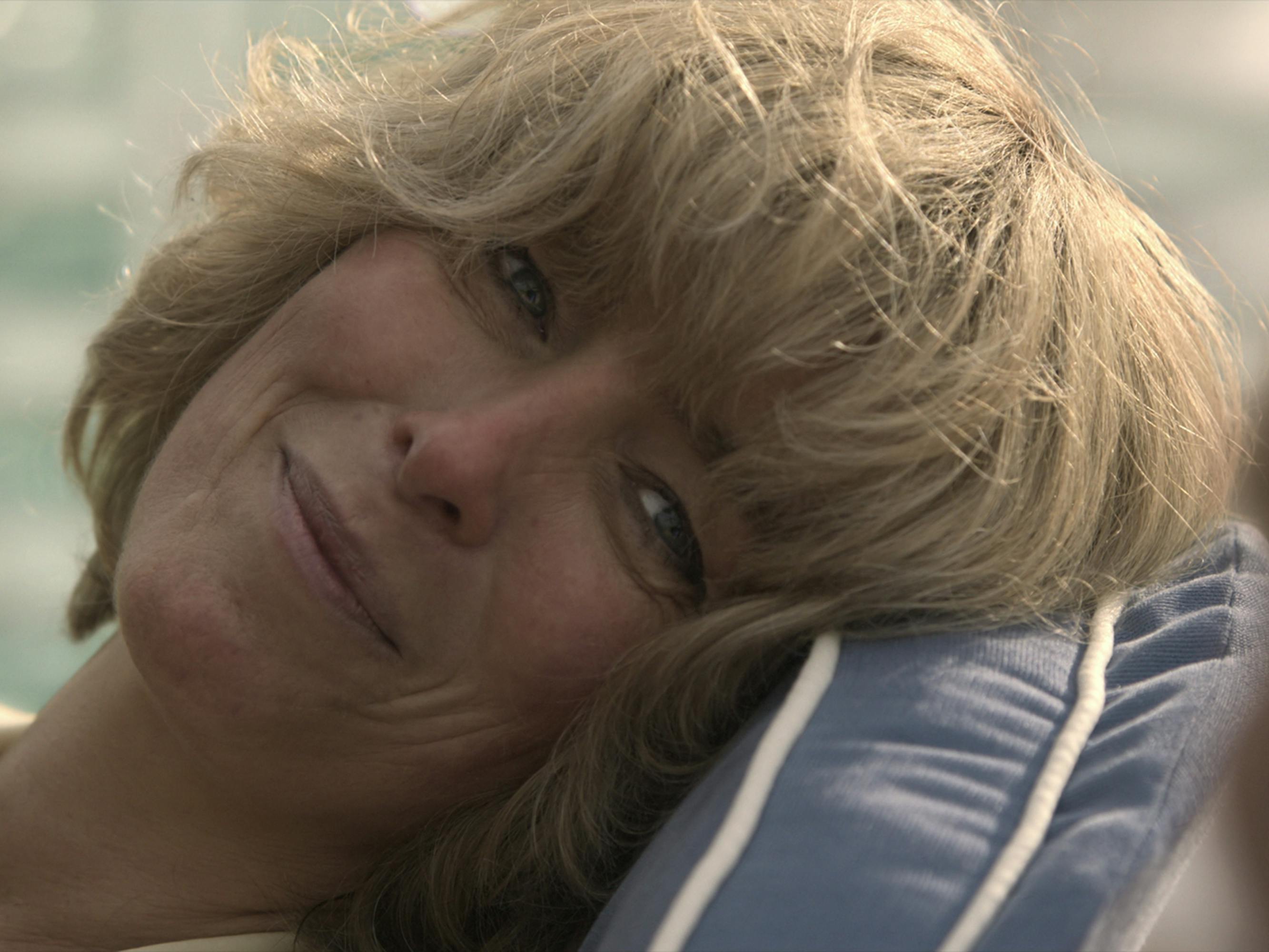 Camilla Parker Bowles (Olivia Williams) leans against a cushion and stares at someone offscreen lovingly.