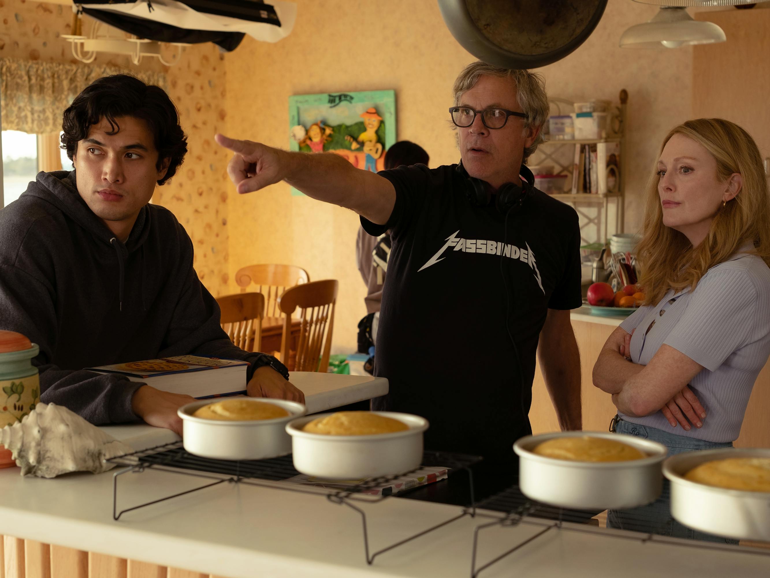 Charles Melton, Todd Haynes, and Julianne Moore behind the scenes in the kitchen. In front of them sit four cakes.