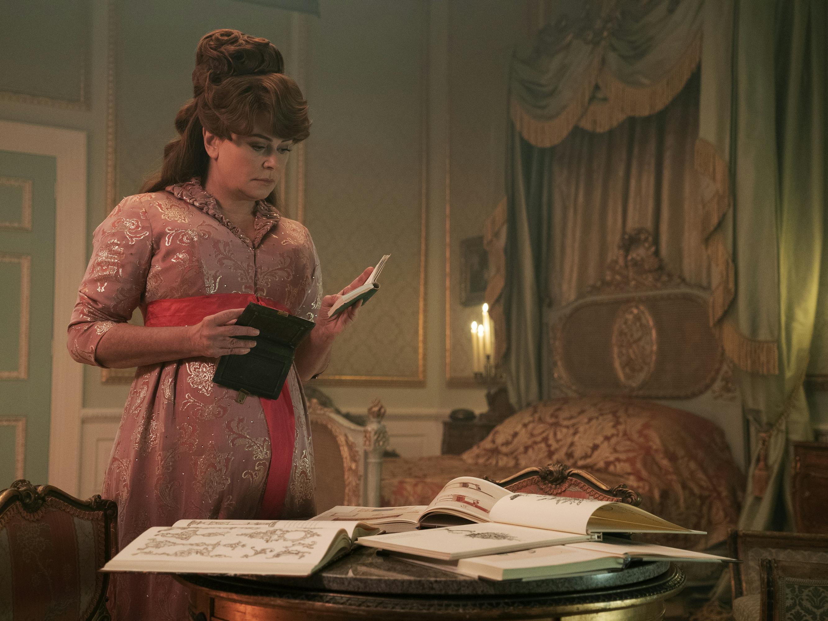 Lady Featherington (Polly Walker) looks over some books in a candle lit room.