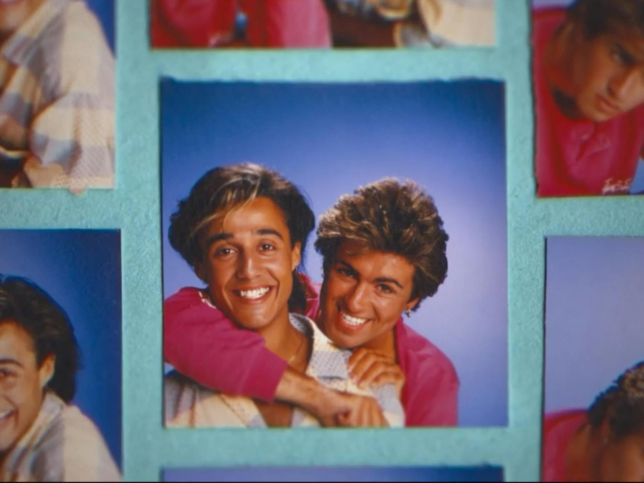 Andrew Ridgeley smiles as George Michael playfully hooks an arm around his neck.