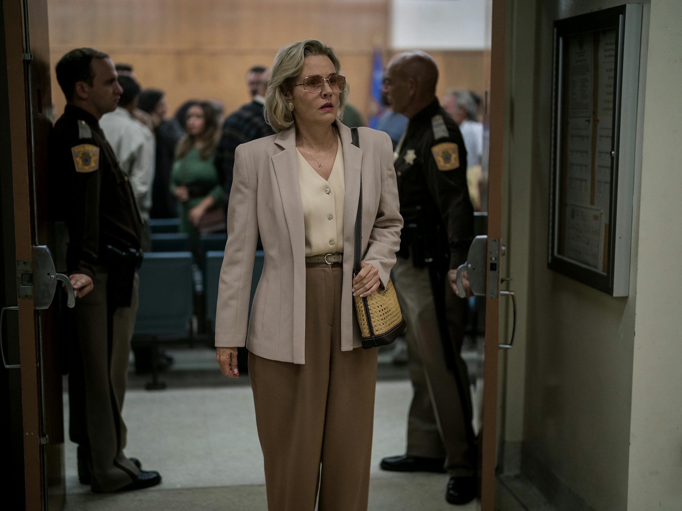 Joyce (Penelope Ann Miller) wears brown pants and a blazer and leaves a courtroom.