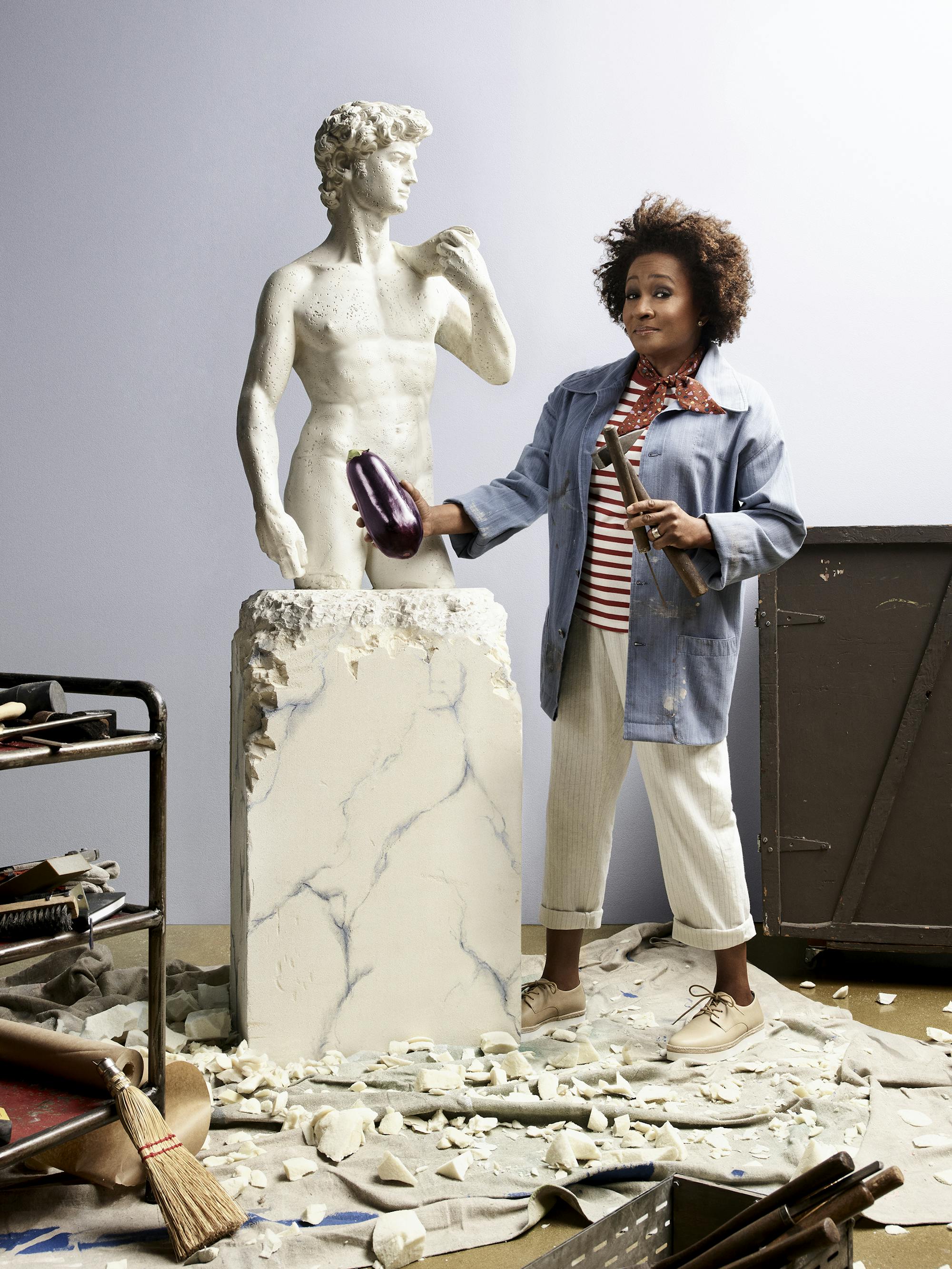 Wanda Sykes holds an eggplant against a stone bust of a Grecian man.