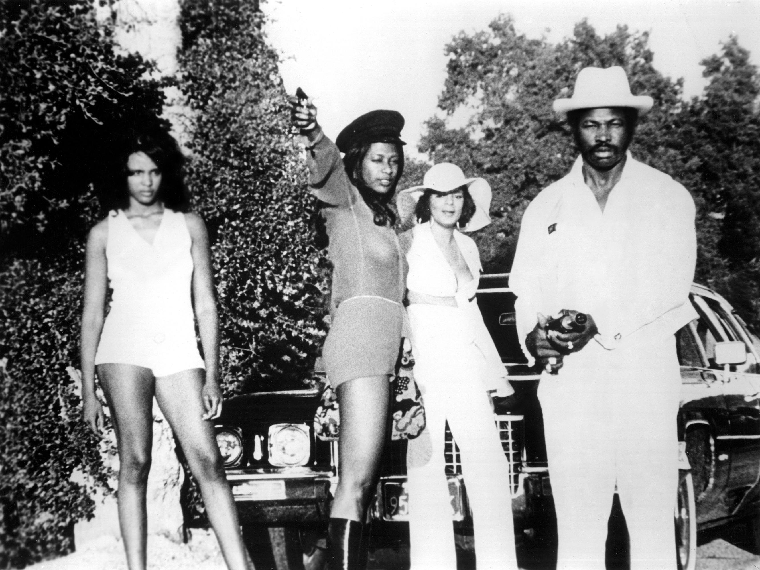 Dolemite (Rudy Ray Moore) and the Dolemite callgirls stand outside a slick black car.