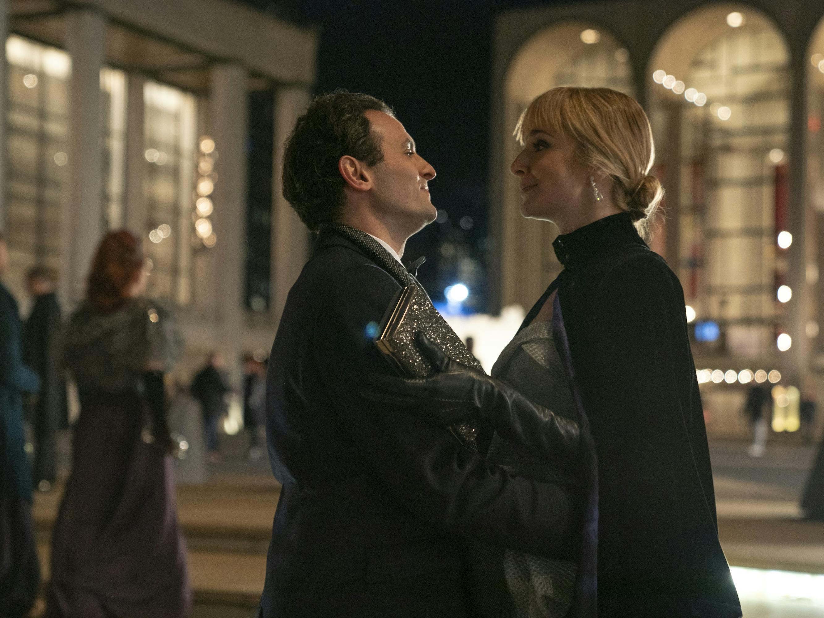 Arian Moayed and Caitlin FitzGerald stand outside Lincoln Center. Moayed and FitzGerald wear black coats, and FitzGerald wears leather gloves.