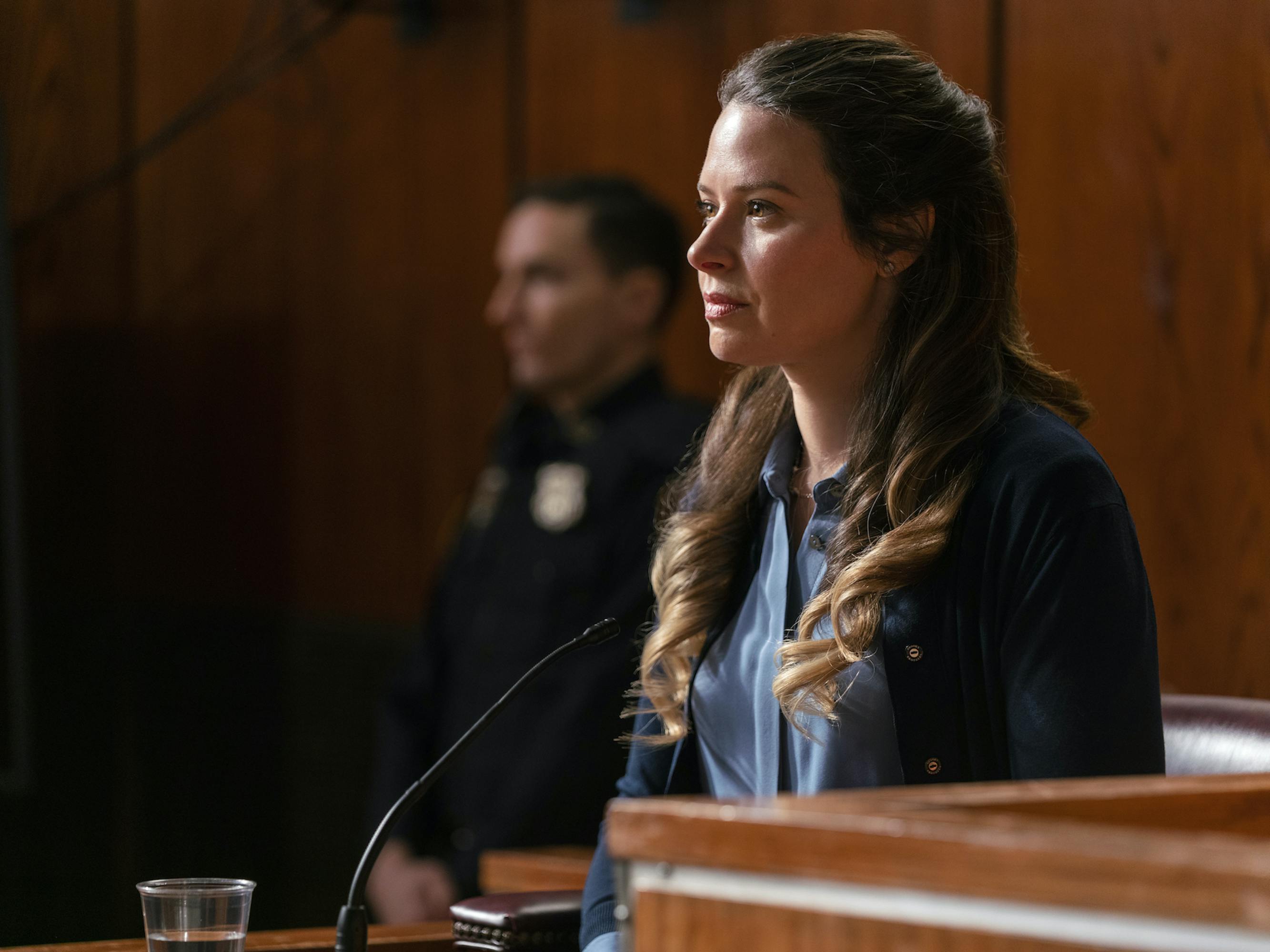 Katie Lowes wears a black top as she takes the stand in a courtroom. 