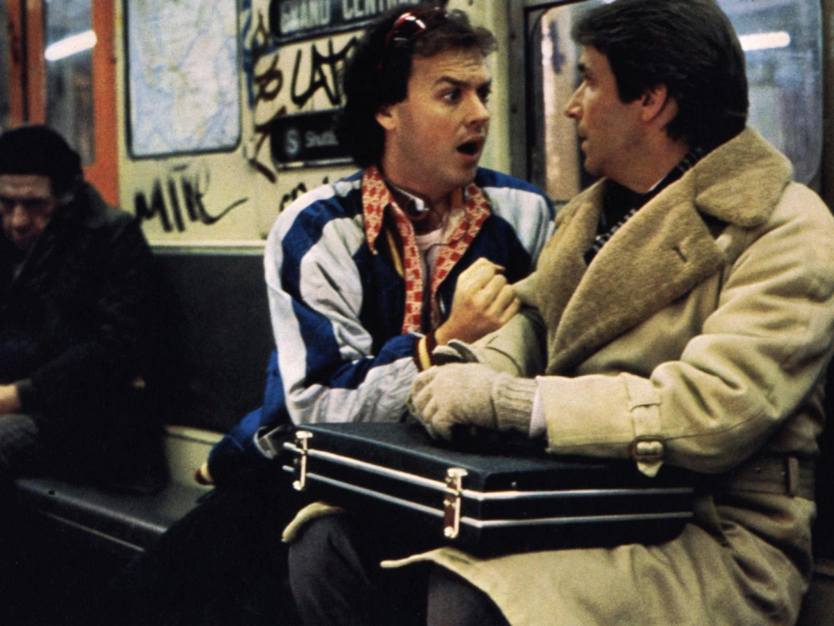Bill Blazejowski (Michael Keaton) and Chuck Lumley (Henry Winkler) in Night Shift. They sit on a train, and Keaton looks at Winkler with urgency. Winkler lies a black briefcase across his lap.