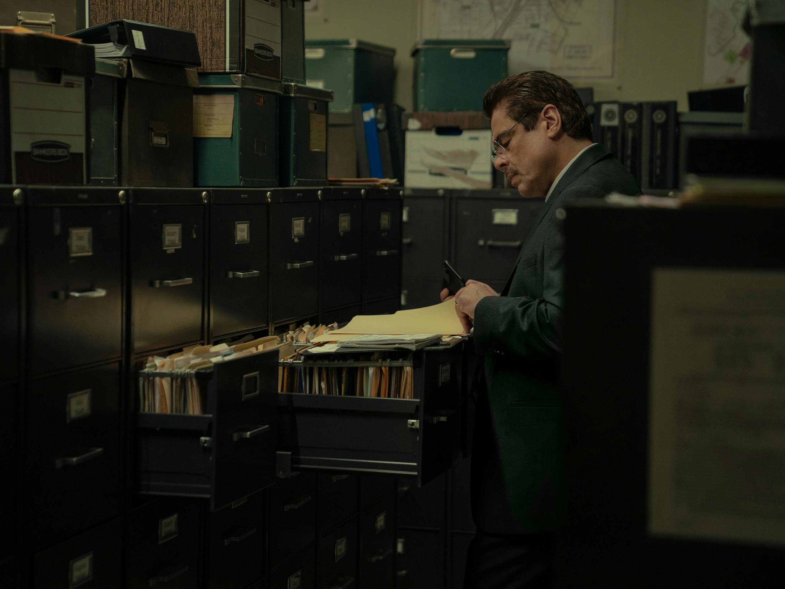 Tom Nichols (Benicio del Toro) studies some files in a darkened office.