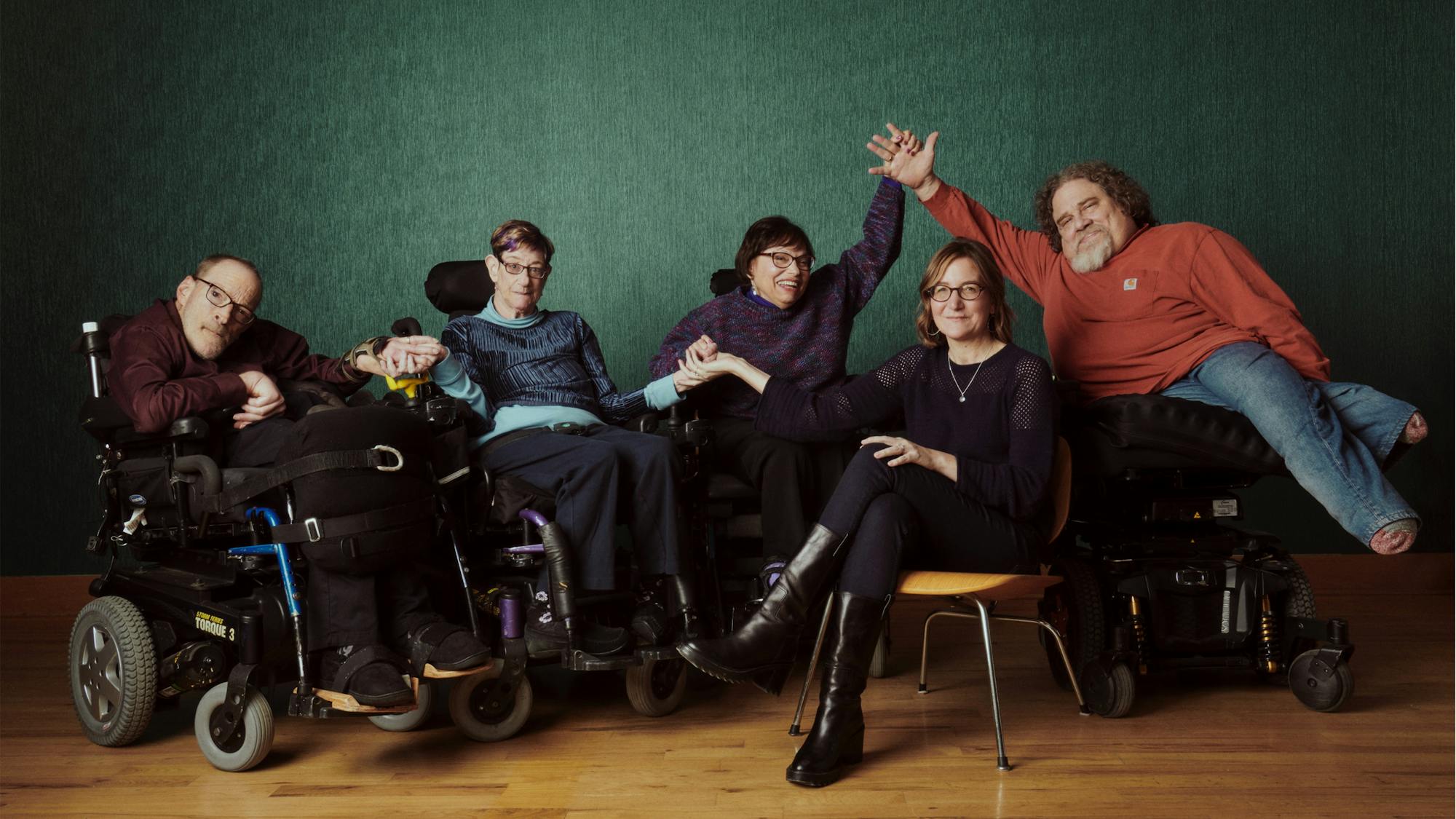 The group holds hands in front of a green backdrop, with Heumann and LeBrecht looking especially celebratory.