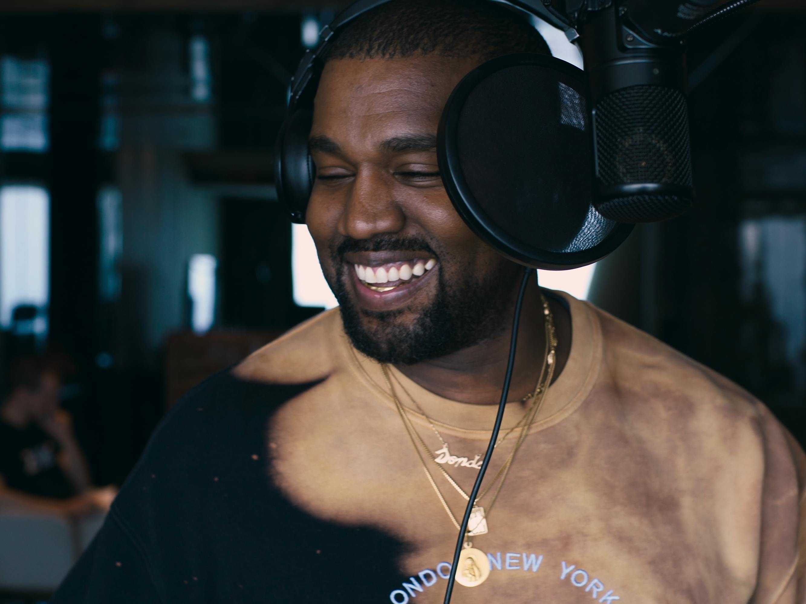 Ye wears a tan shirt and earphones and looks very happy as he recorsd.