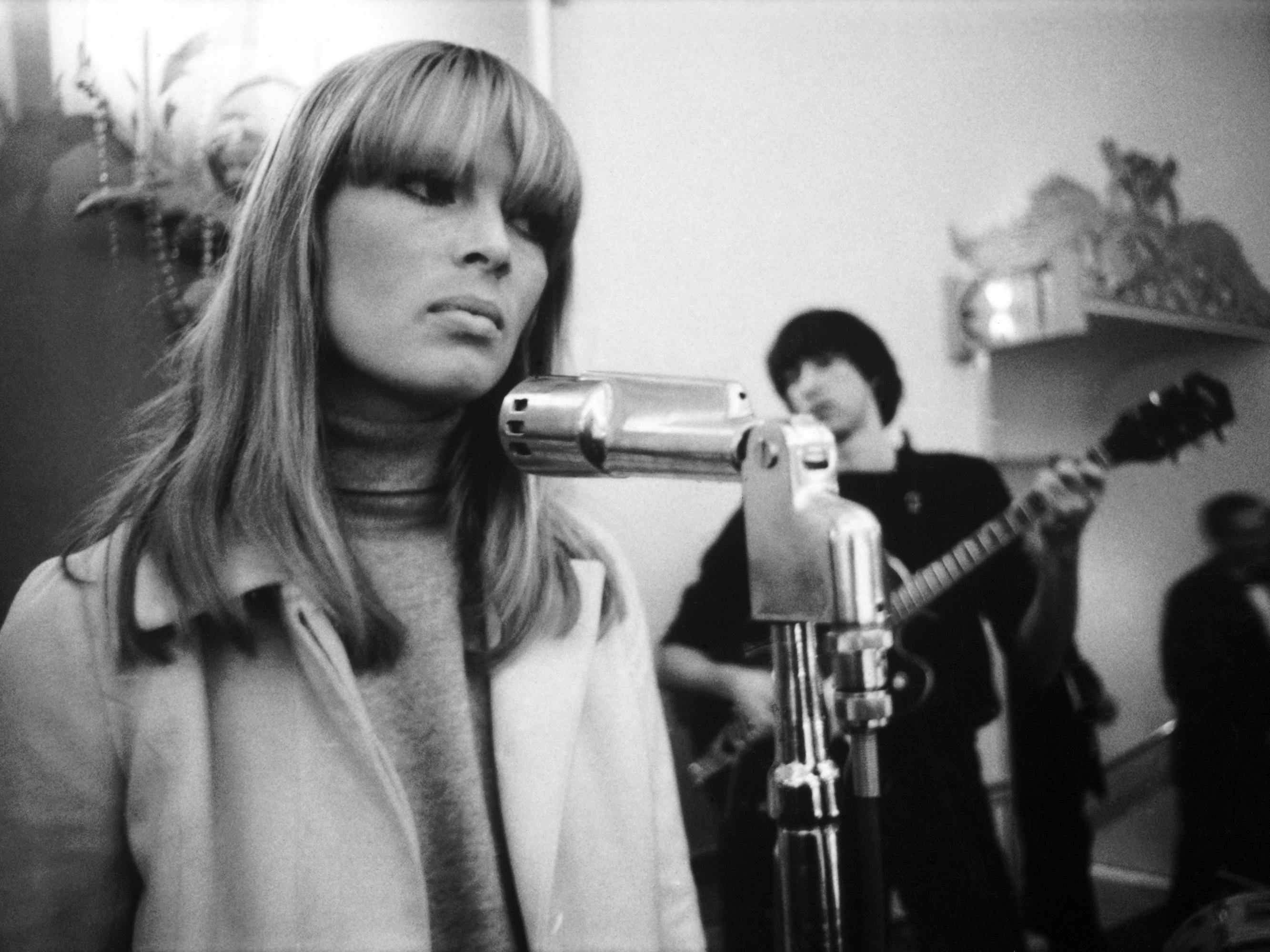 Nico wears a turtleneck and sings into a mic in this black-and-white image.