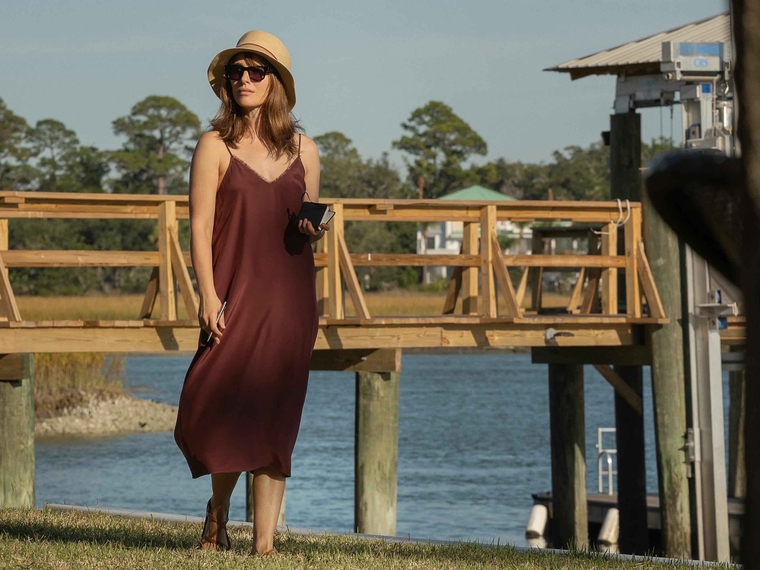 Natalie Portman wears a maroon dress and walks on a dock.