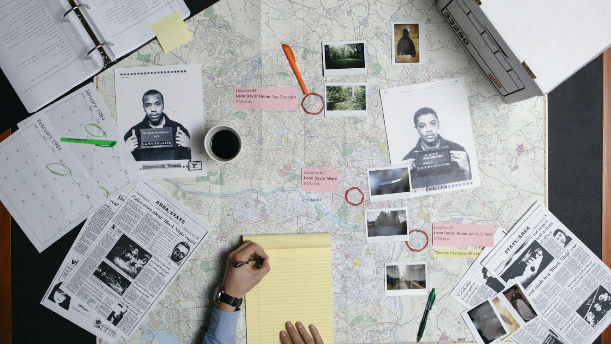 A shot from above of the work being done at the Innocence Project, as told by The Innocence Files. A man writes on a yellow legal pad atop a spread of maps, images, pens, notebooks, and other tools.