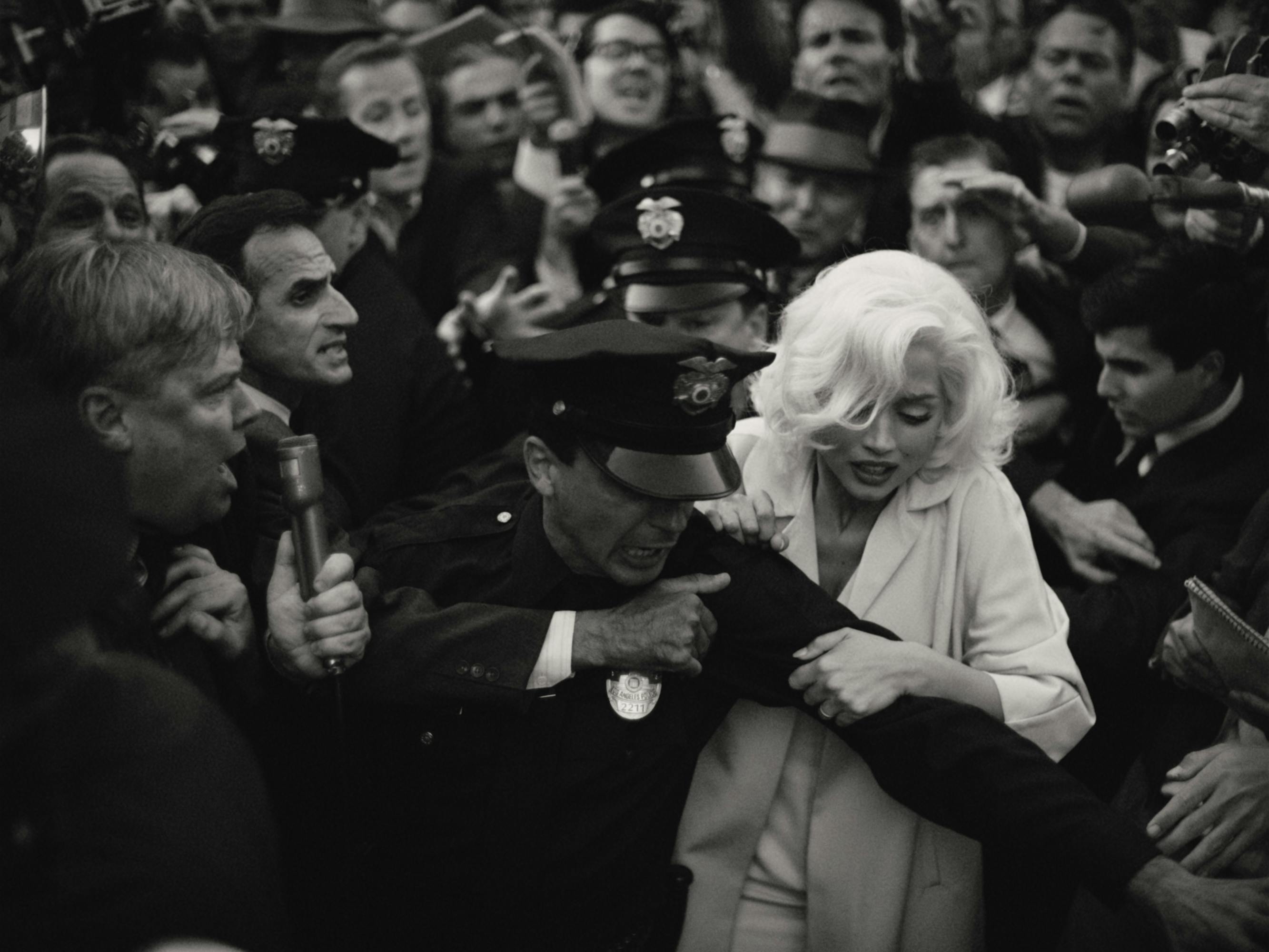 Marilyn Monroe (Ana de Armas) se abre paso entre una multitud hambrienta con la ayuda de un oficial de policía.