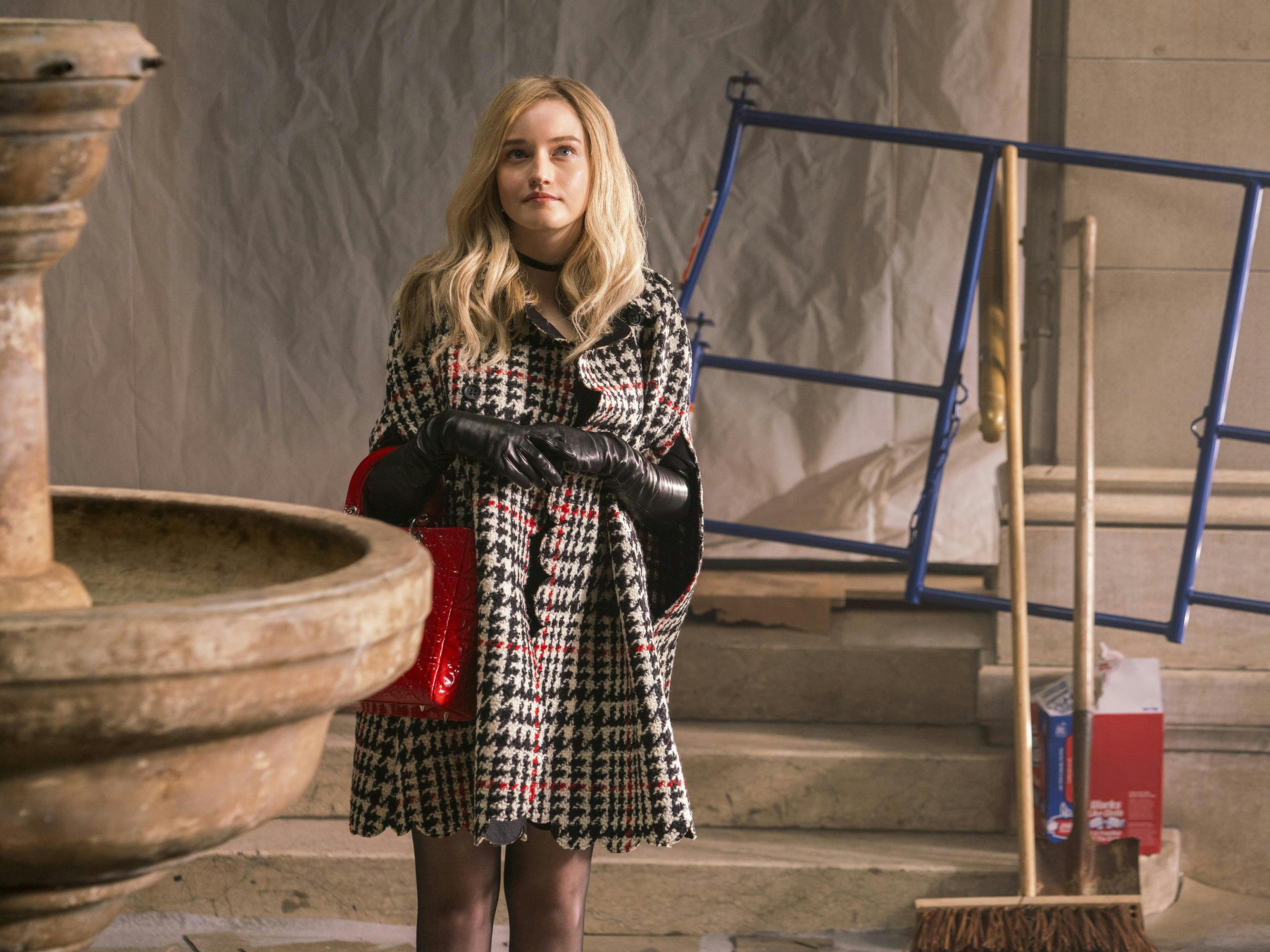 Anna Delvey (Julia Garner) wears a houndstooth poncho and stands in a construction site looking hopeful.