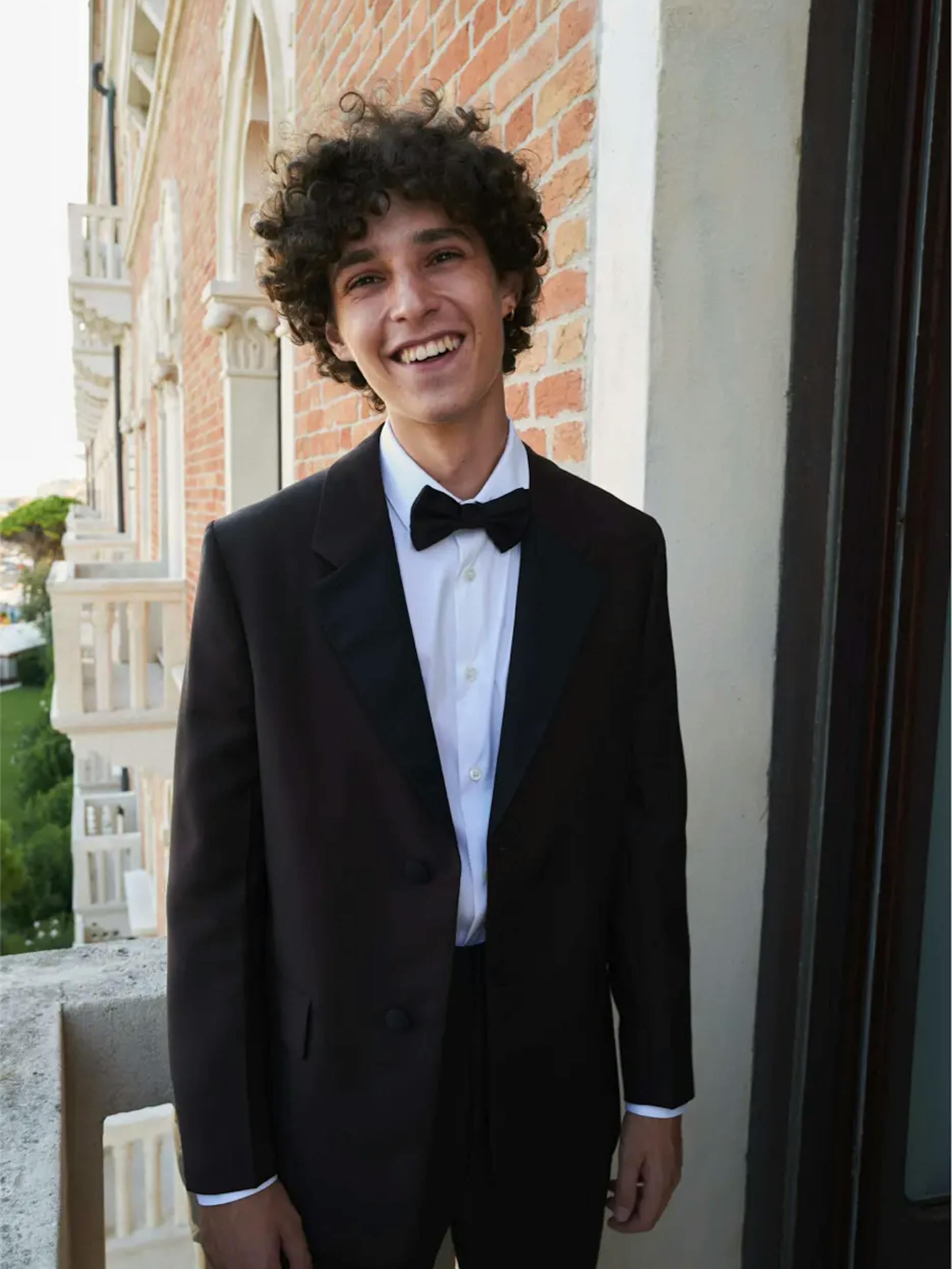 Filippo Scotti wears a tux and bowtie and smiles as he stands on a balcony.