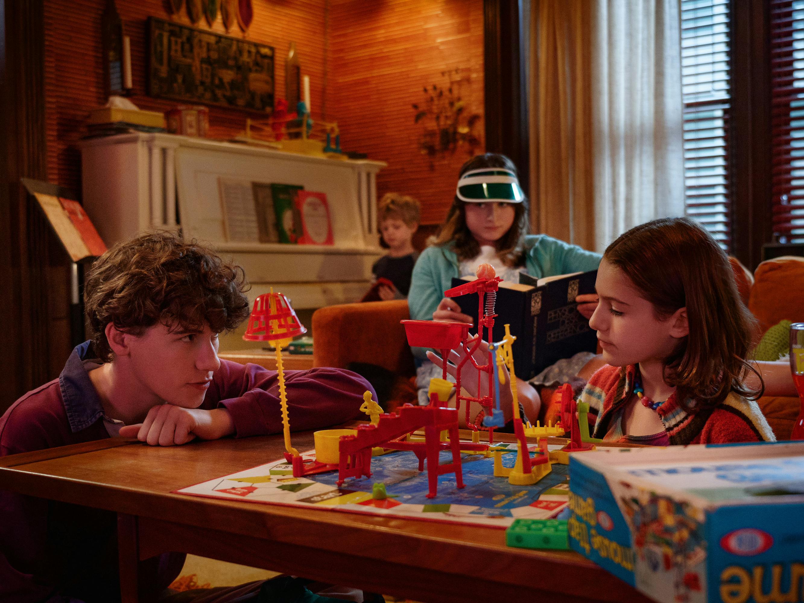 Heinrich (Sam Nivola), Wilder (Henry/Dean Moore), Denise (Raffey Cassidy), and Steffie (May Nivola) sit together in a cozily-lit room, strewn with toys.