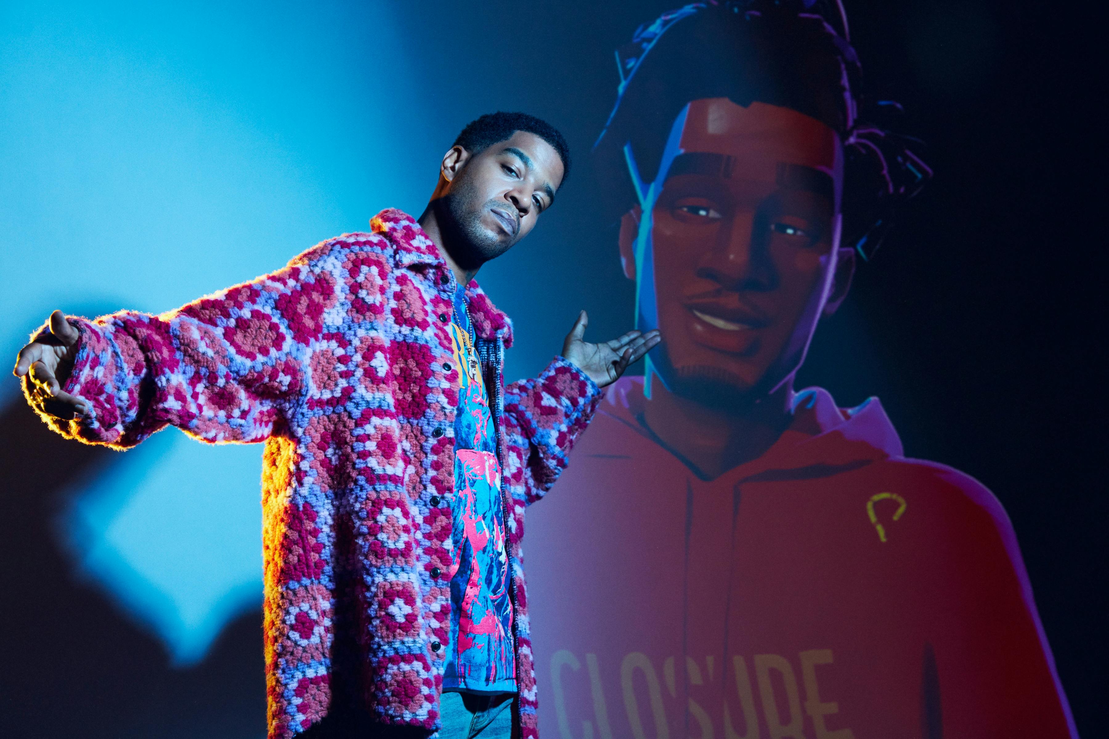 Jabari (Scott Mescudi) wears an incredible pink jacket and stands in front of a hologram of his character.