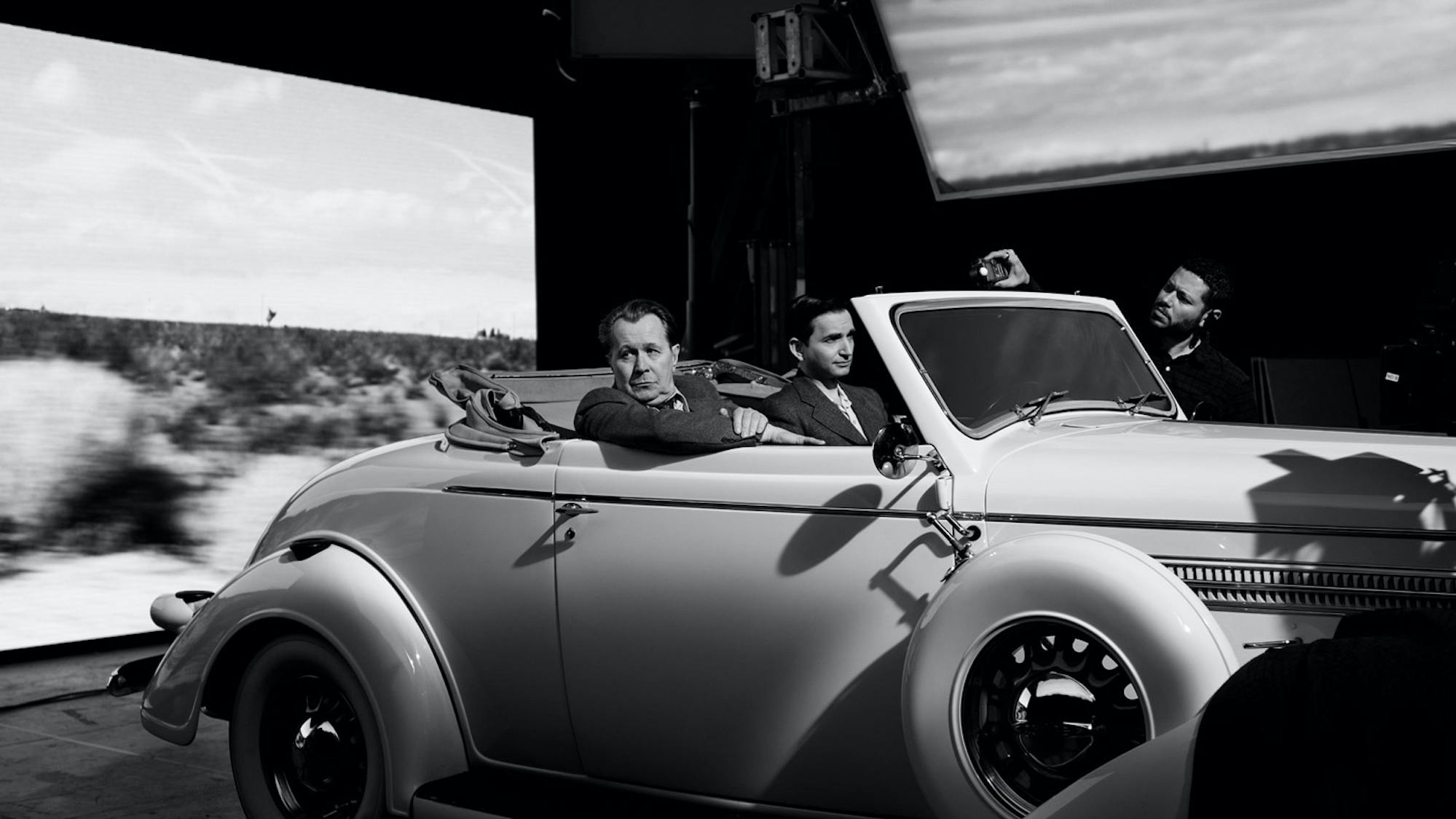 Oldman and Persaud pictured in an open-top automobile with footage of California scenery rolling by on screens around them.