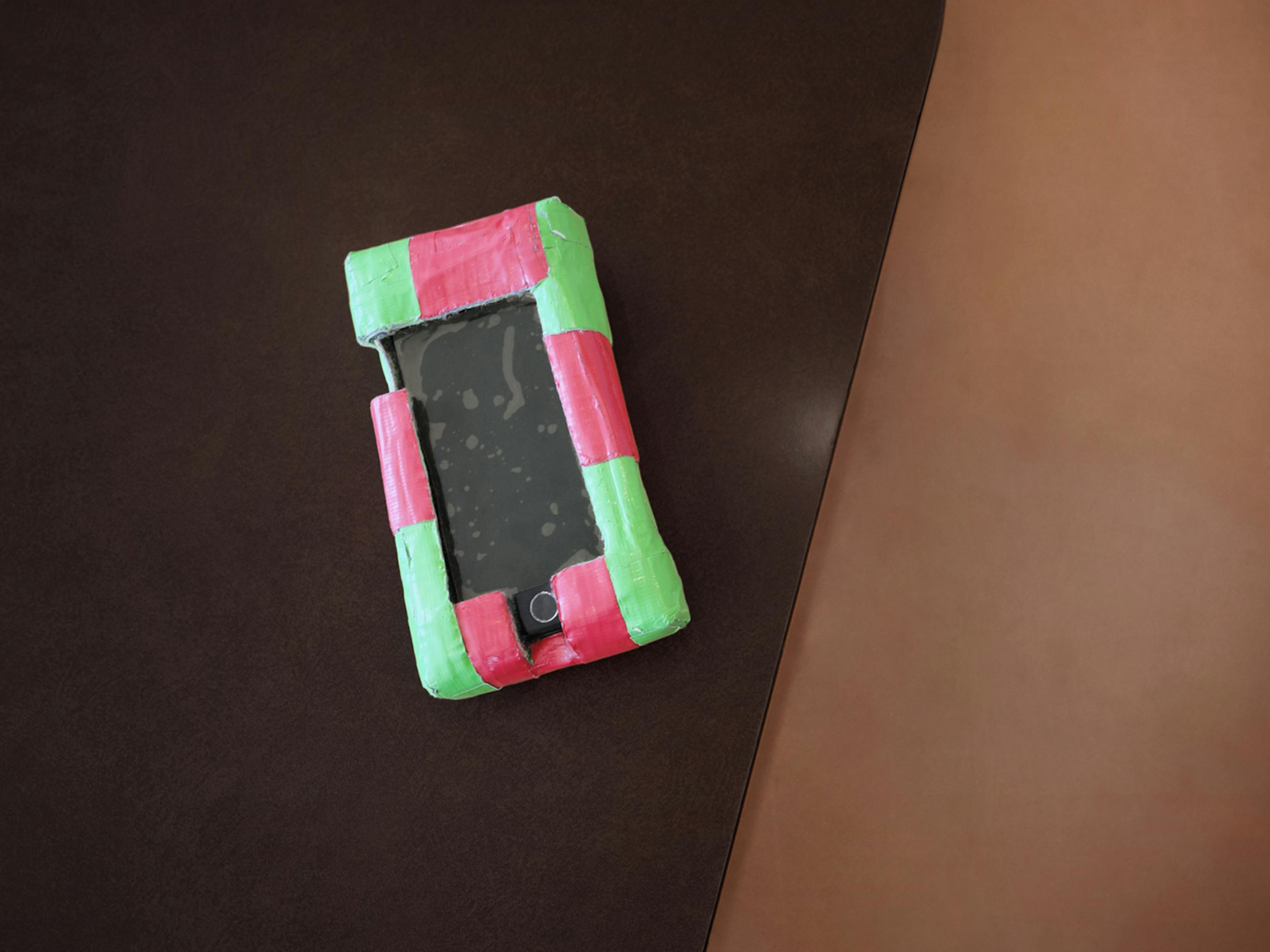 An old iphone with a green and pink case.