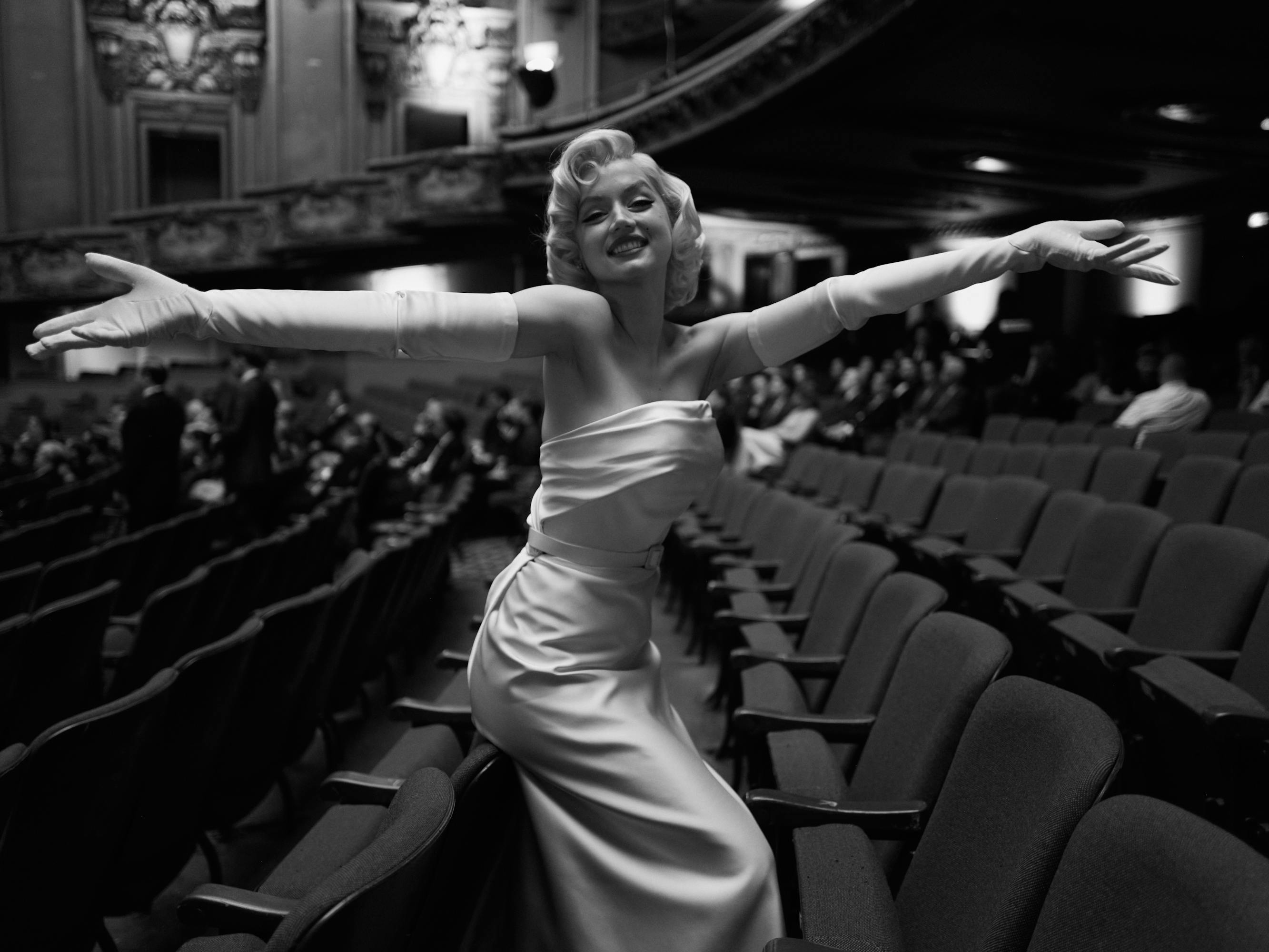 Marilyn Monroe (Ana de Armas) wears a satin dress and gloves and stands in an empty theater smiling.