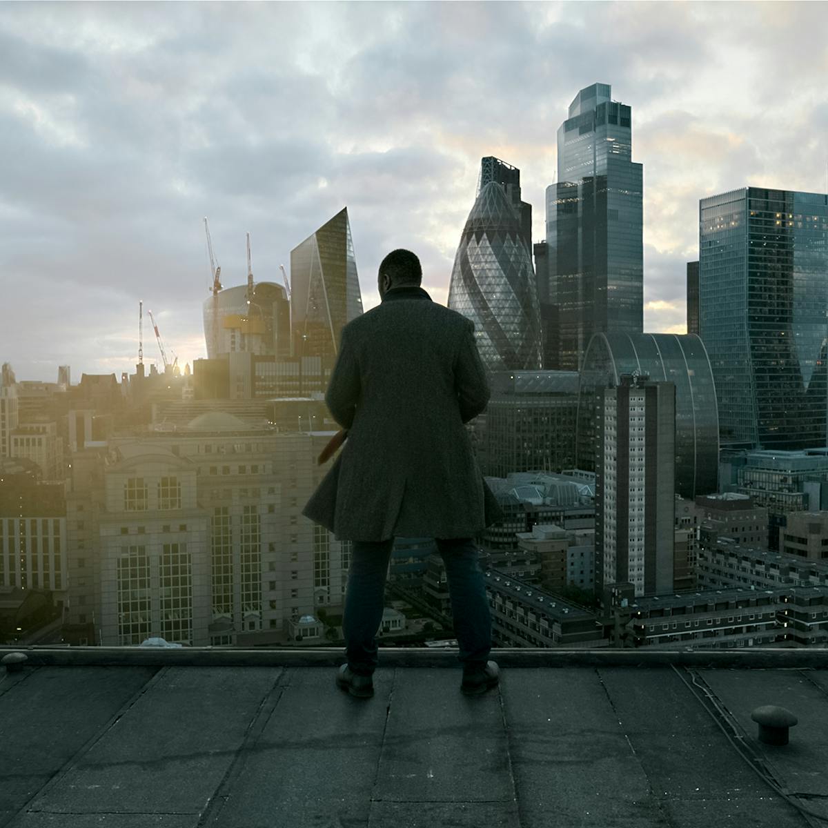John Luther (Idris Elba) stands on a roof overlooking London, as the sun crests behind the skyline.