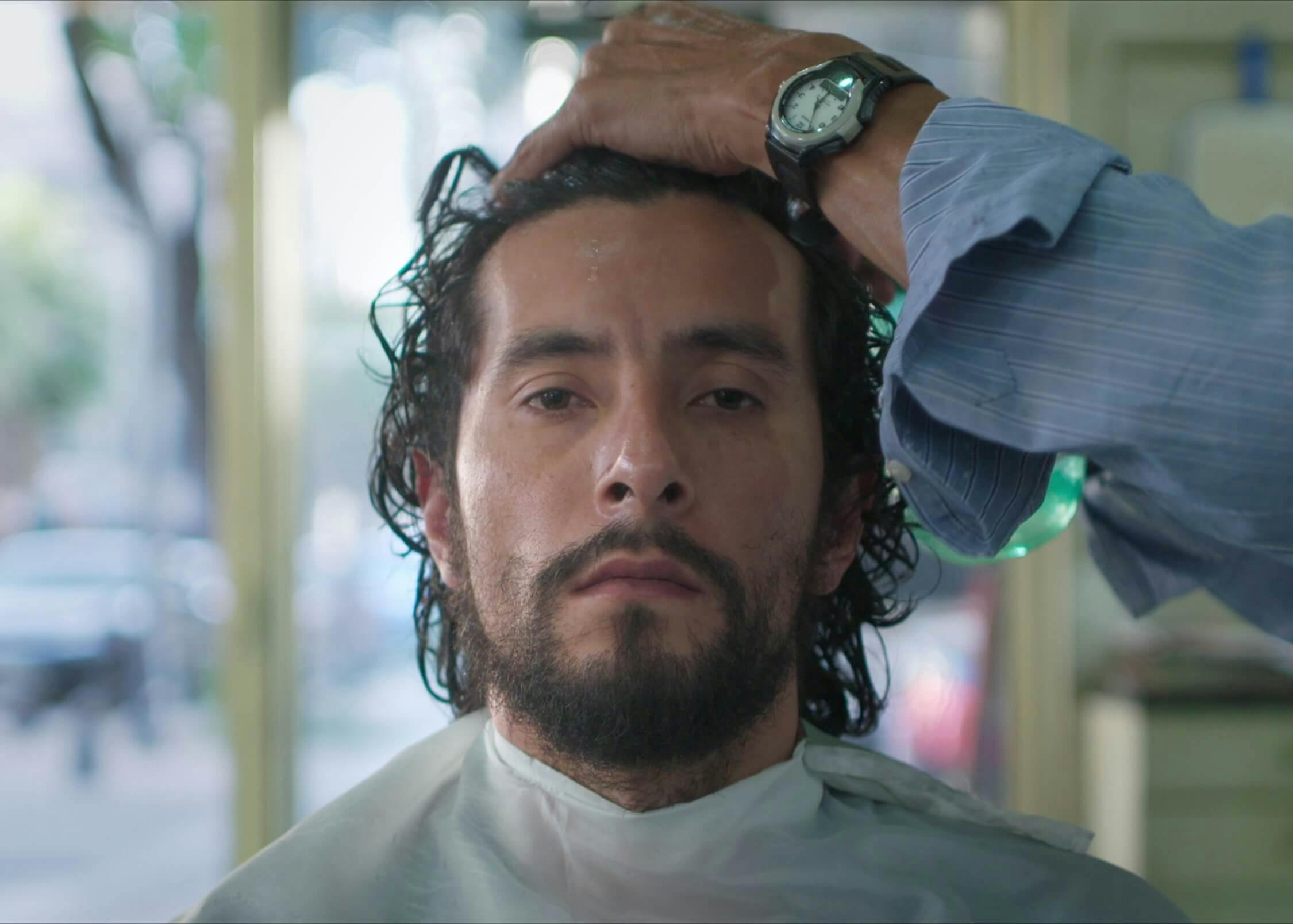 A close-up shot of a man getting his hair cut, but another man wearing a watch and blue shirt.