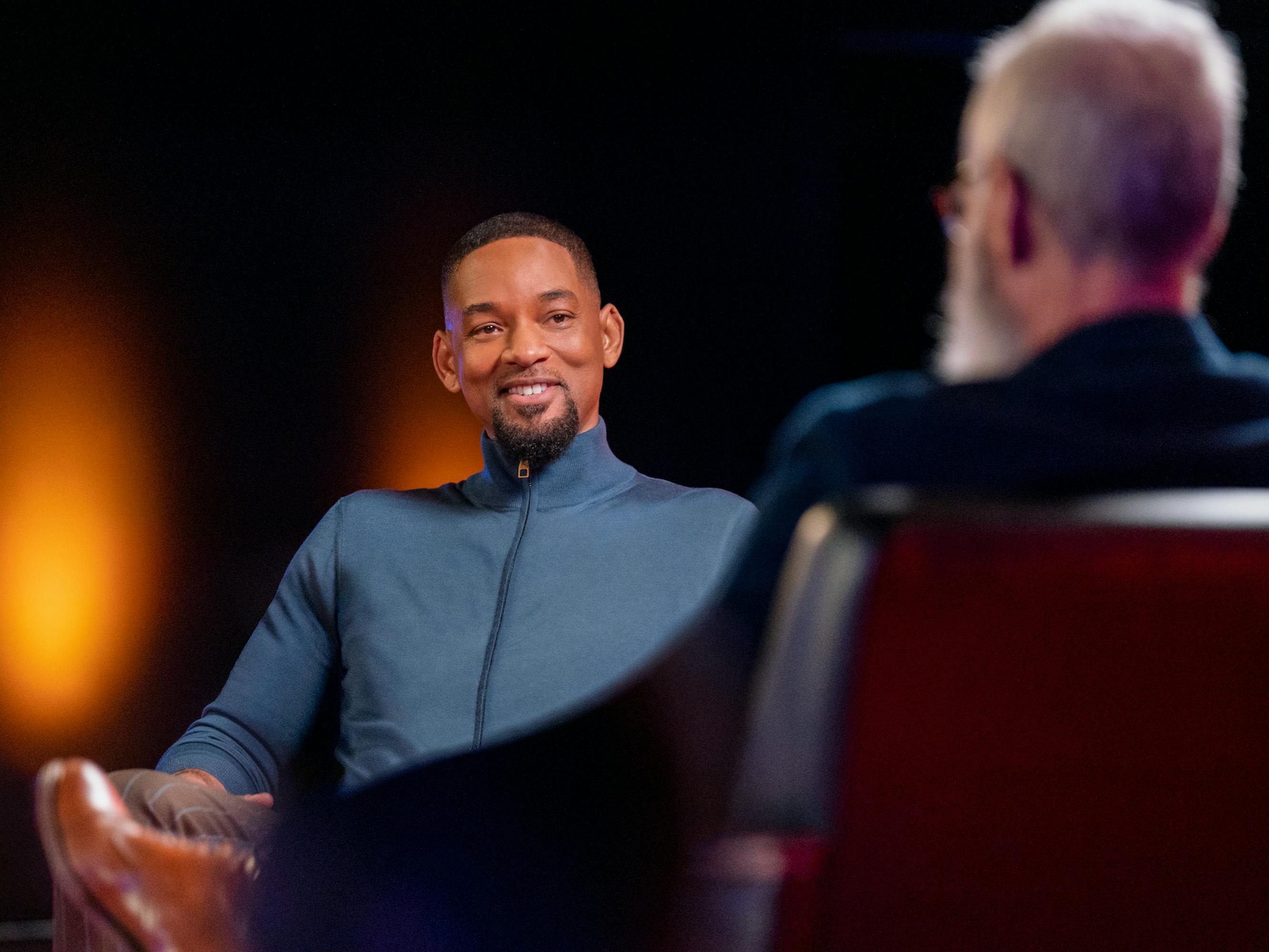 Will Smith and David Letterman talk in a dimly lit room. Smith wears a navy top.