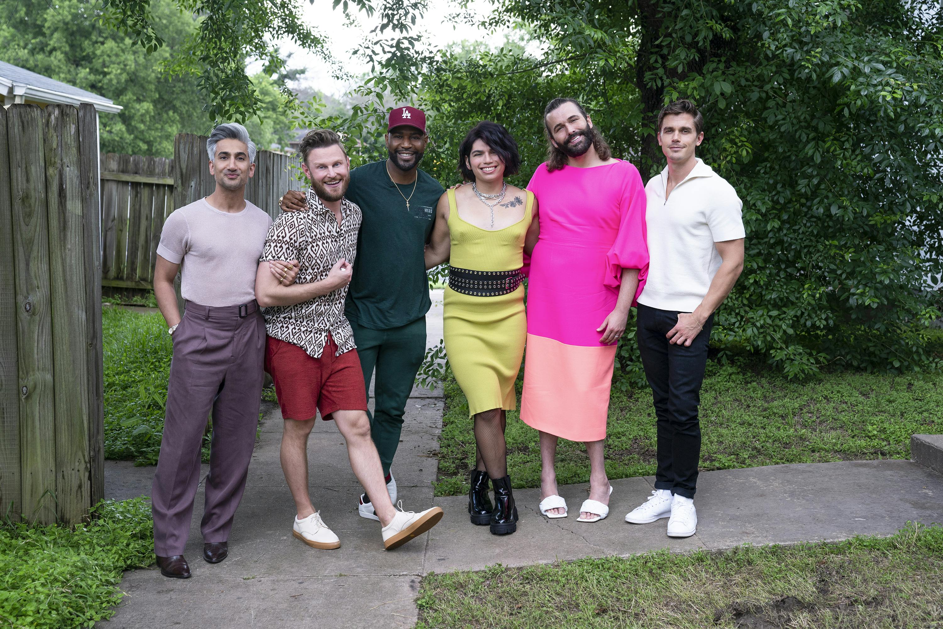 Tan France, Bobby Berk, Karamo Brown, Angel Flores, Jonathan Van Ness, and Antoni Porowski stand together outside in a green spot.