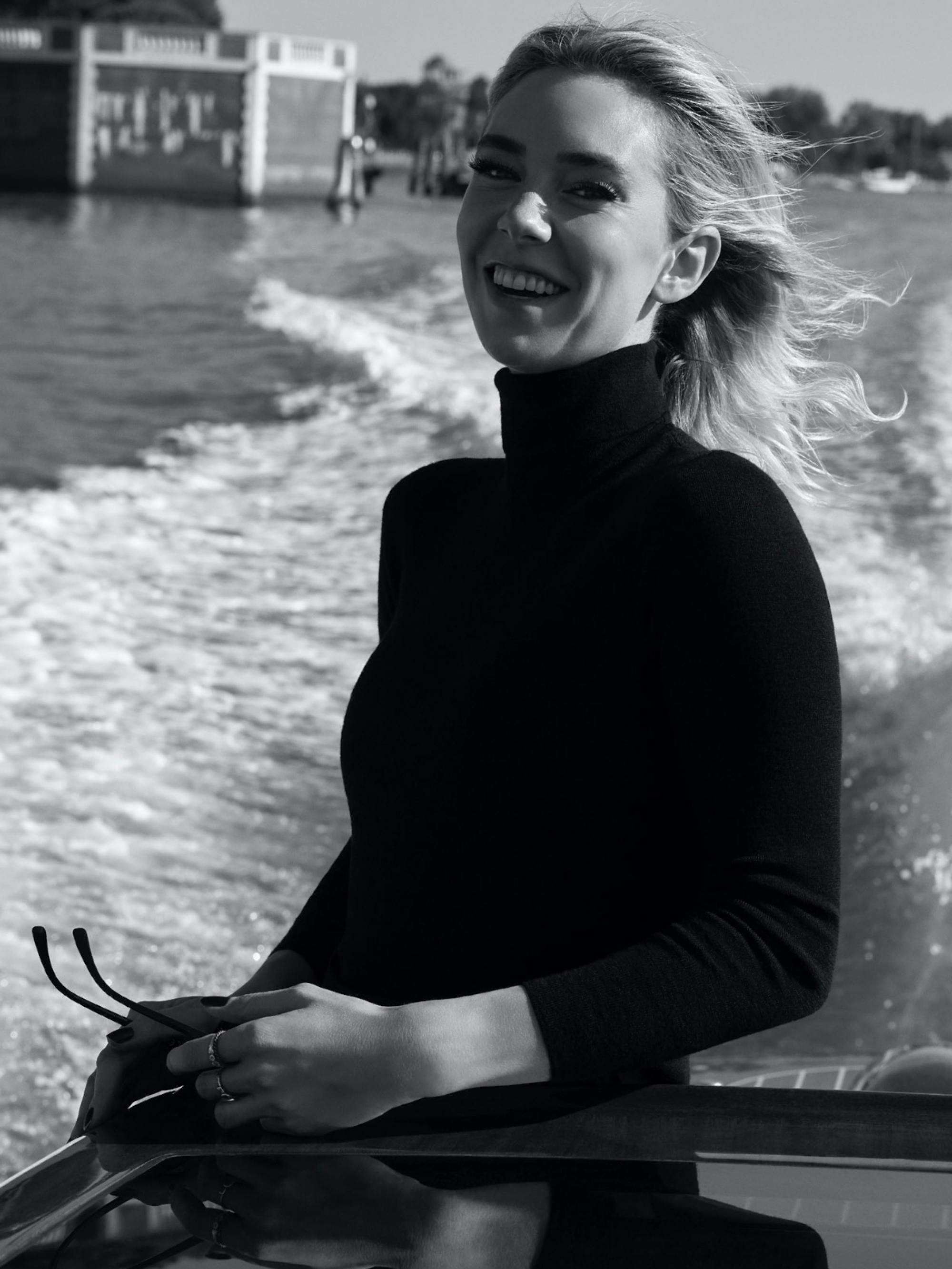 Vanessa Kirby smiles as she stands on a boat, her hair blowing in the wind.