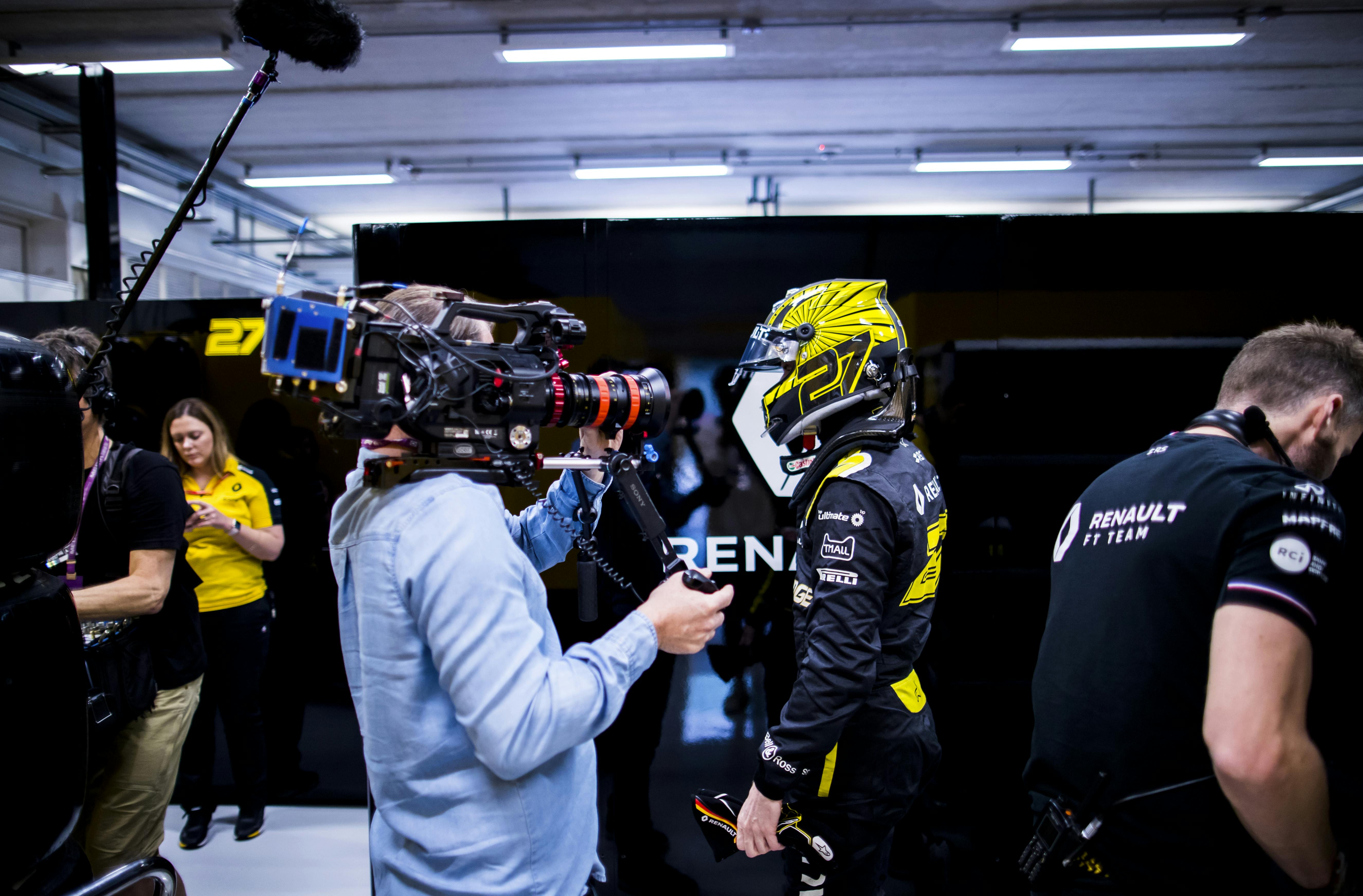 A cameraman interviews a race car driver dressed in black and yellow.