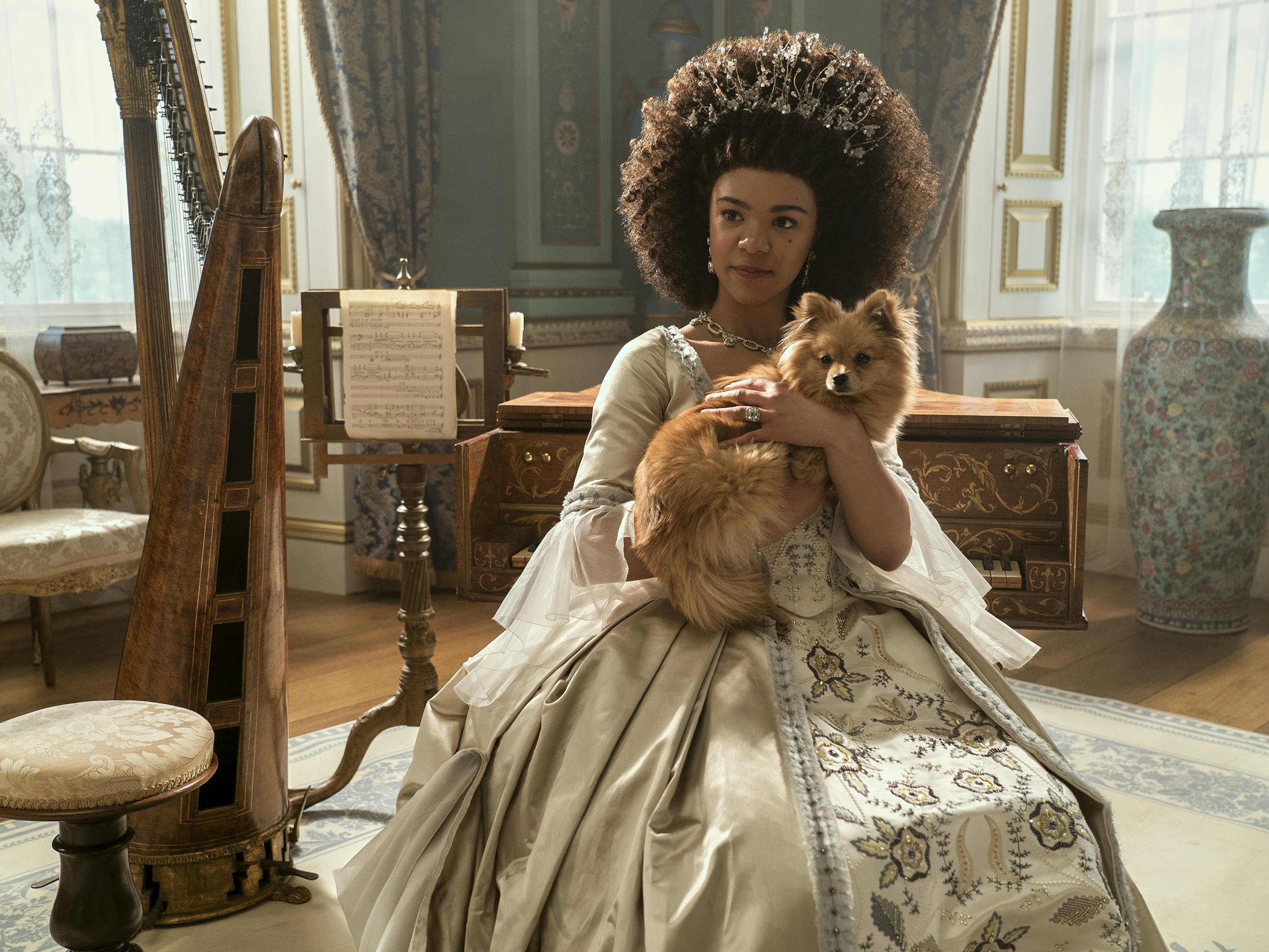 Young Queen Charlotte (India Amarteifio) holds her dog. In the background is a harp and some sheet music.