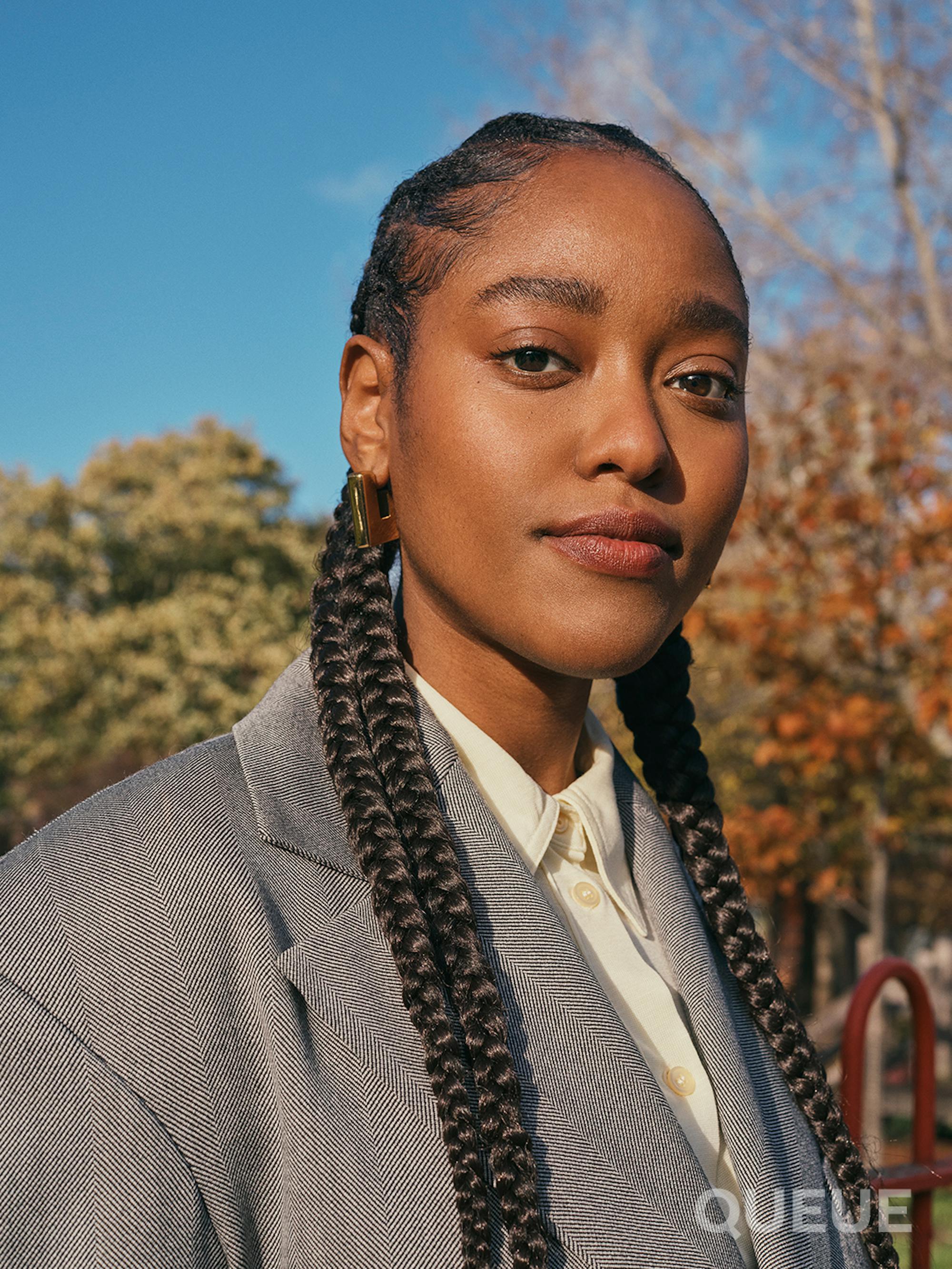 Arsema Thomas wears a white shirt, a gray blazer, and has long braids.